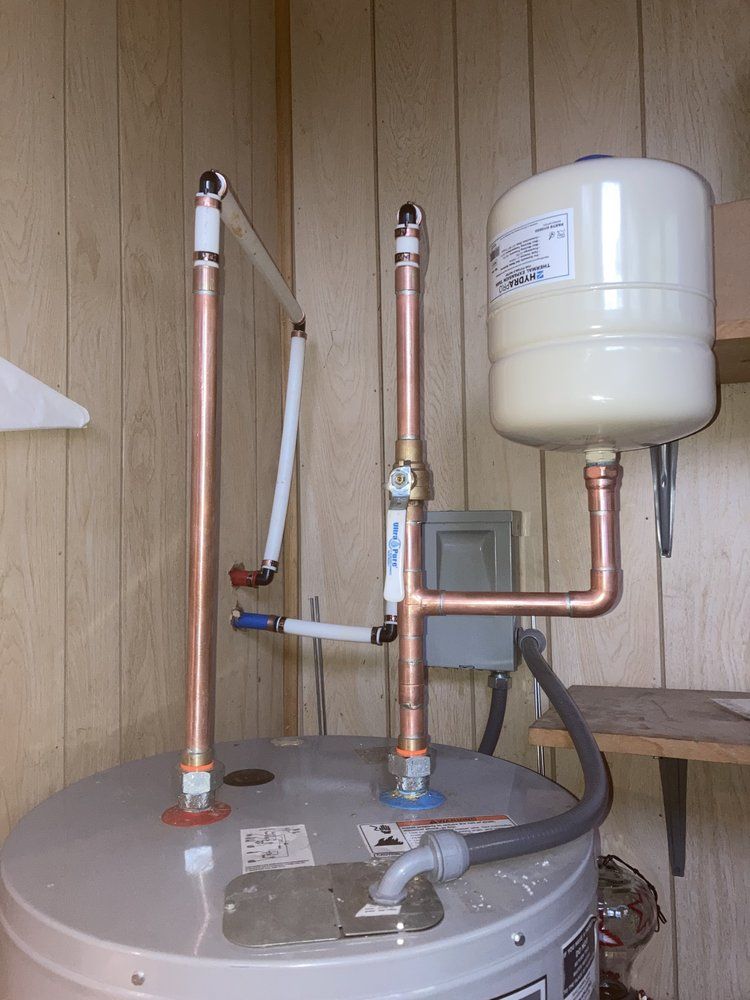 A water heater with copper pipes attached to it is sitting in a room.