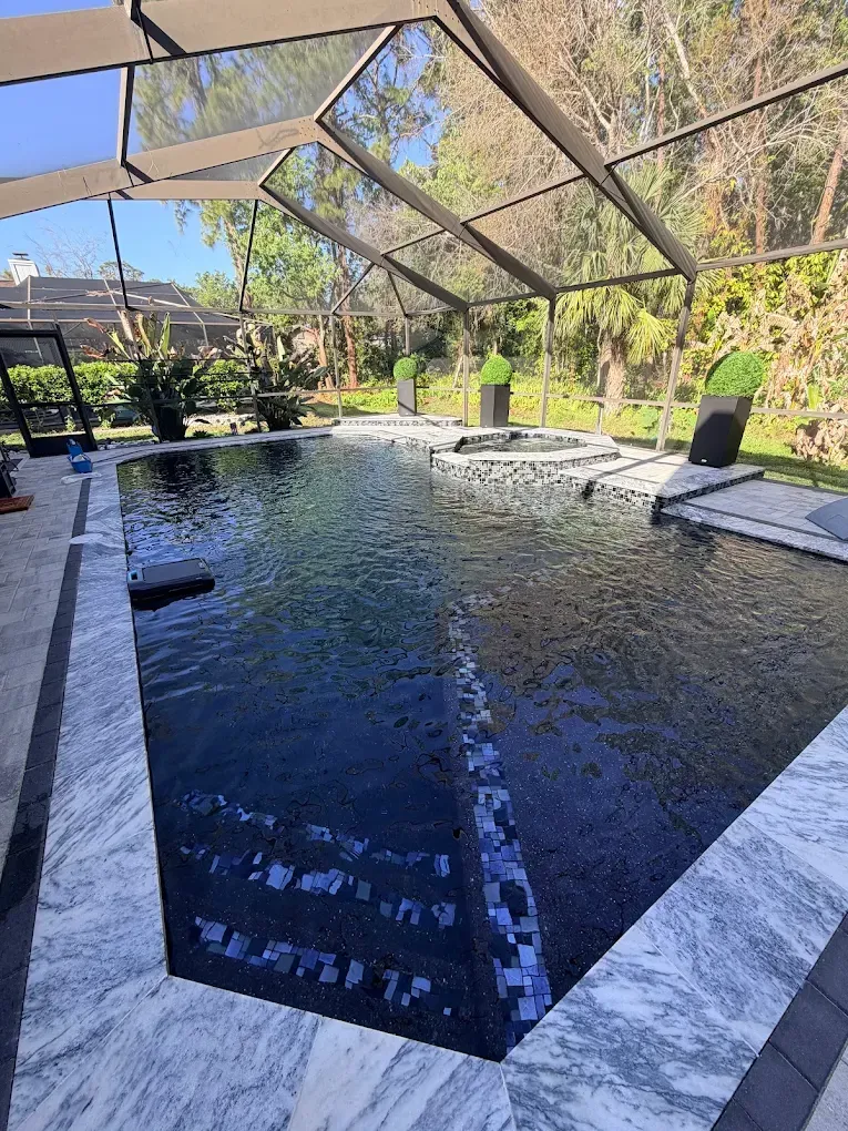 Covered outdoor pool with dark water, white stone edge, and lounge chairs under a screened patio.