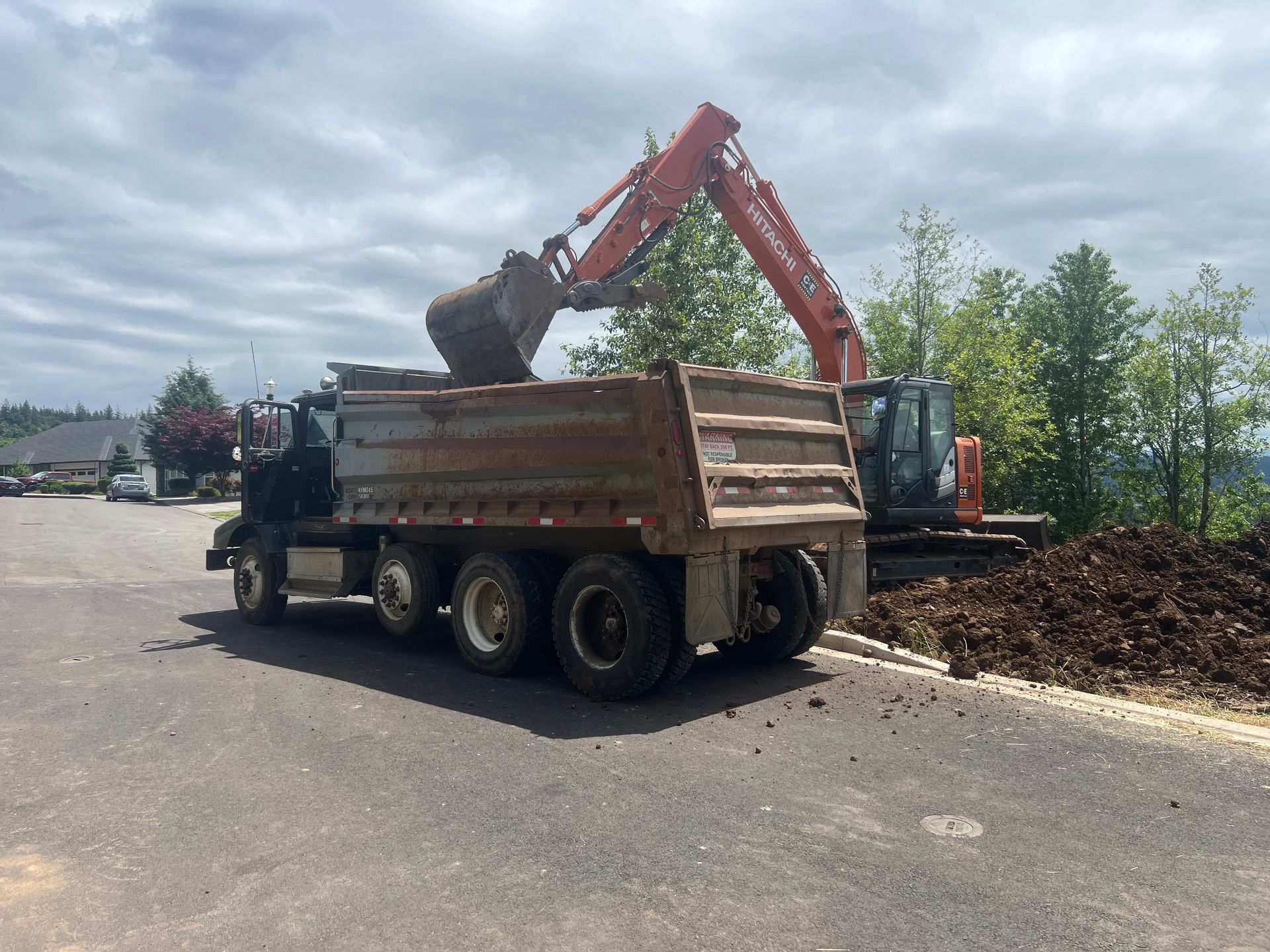 An excavator demolishes a stone building, surrounded by rubble. Bright blue sky overhead.