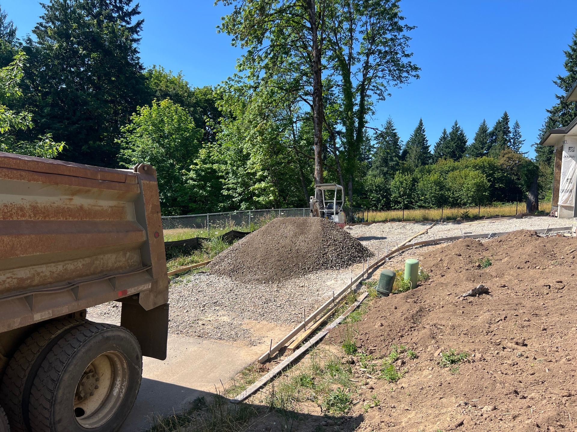 A yellow loader fills a white dump truck with gravel under a partly cloudy blue sky.