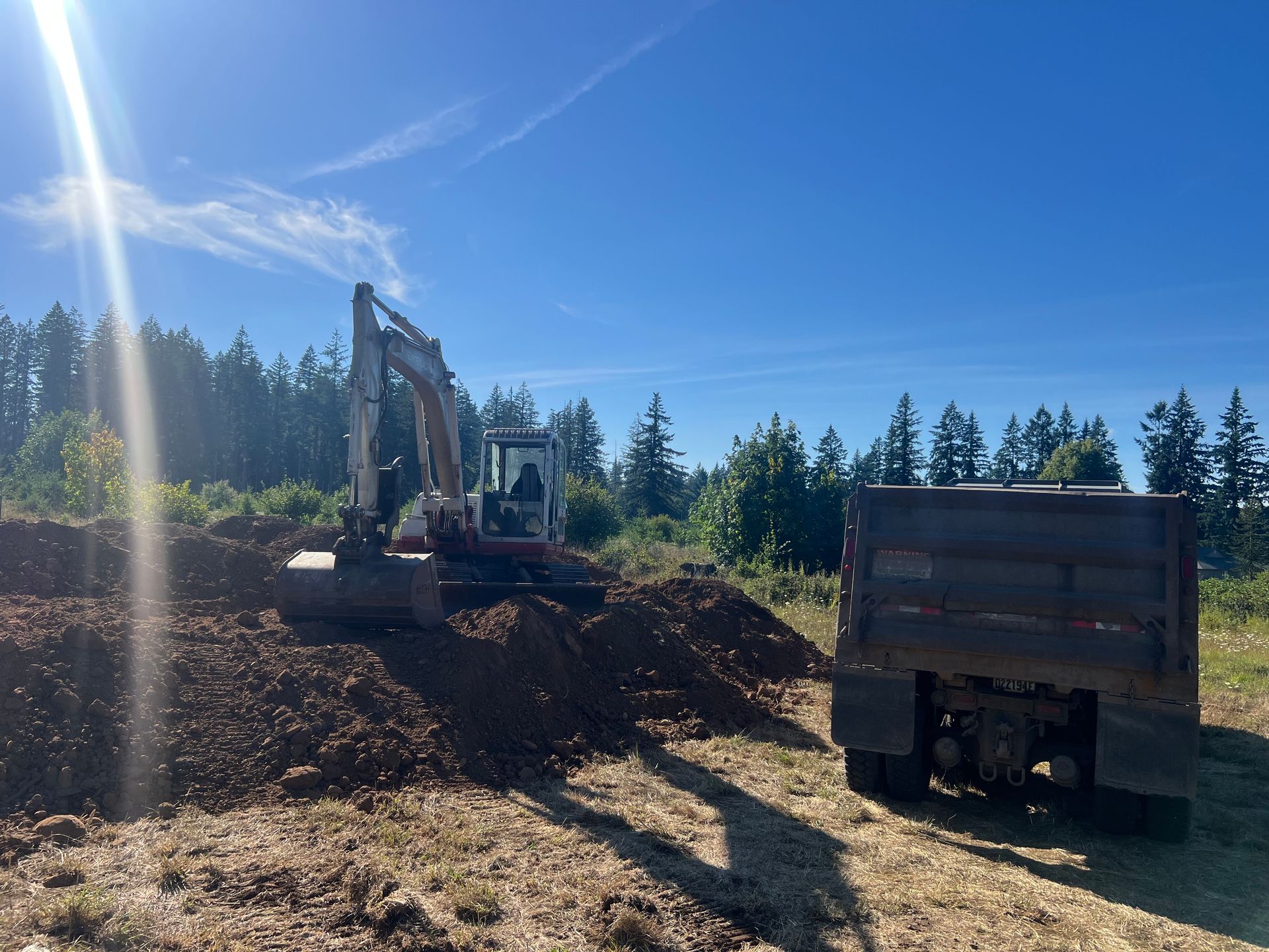 Bulldozer clearing a muddy field near a body of water, under a bright sky.