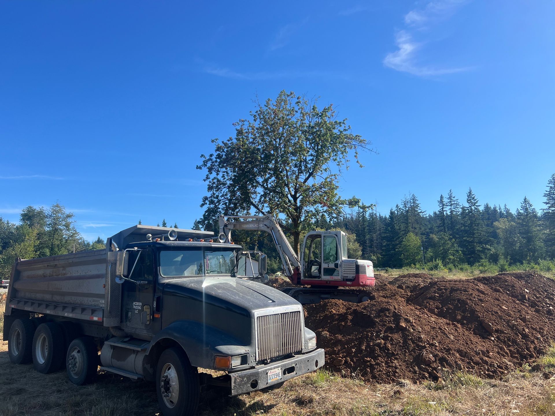 Yellow excavator digging in dirt, with a blue and orange sky in the background.