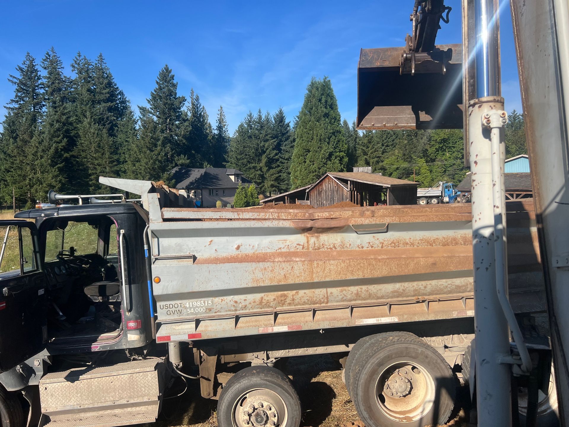 Orange dump truck parked outdoors with a wooded background.