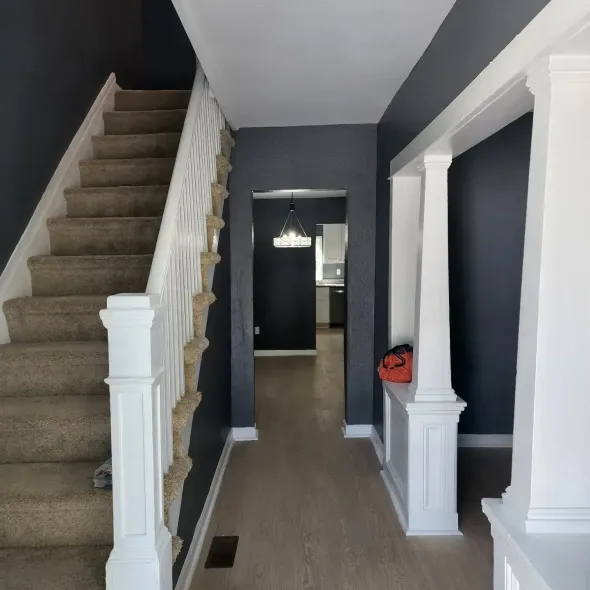 Hallway with staircase on left, dark gray walls, white trim and columns, light wood floors.