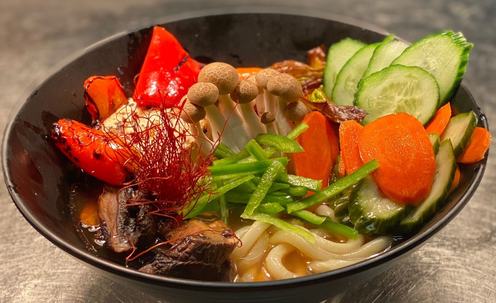 A bowl of noodles with vegetables and mushrooms on a table.