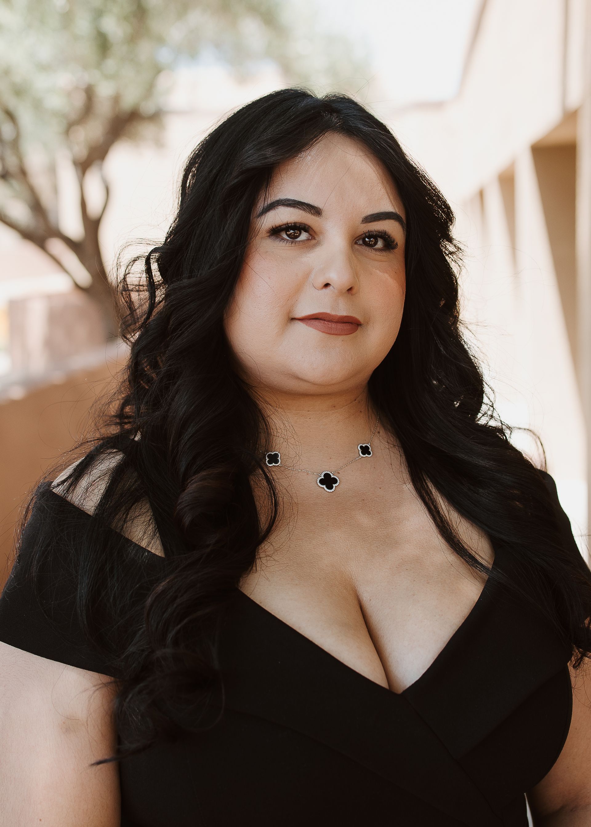 A woman in a black dress and necklace is standing in front of a building.