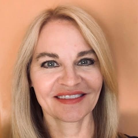 A woman with blonde hair and green eyes is smiling for the camera.