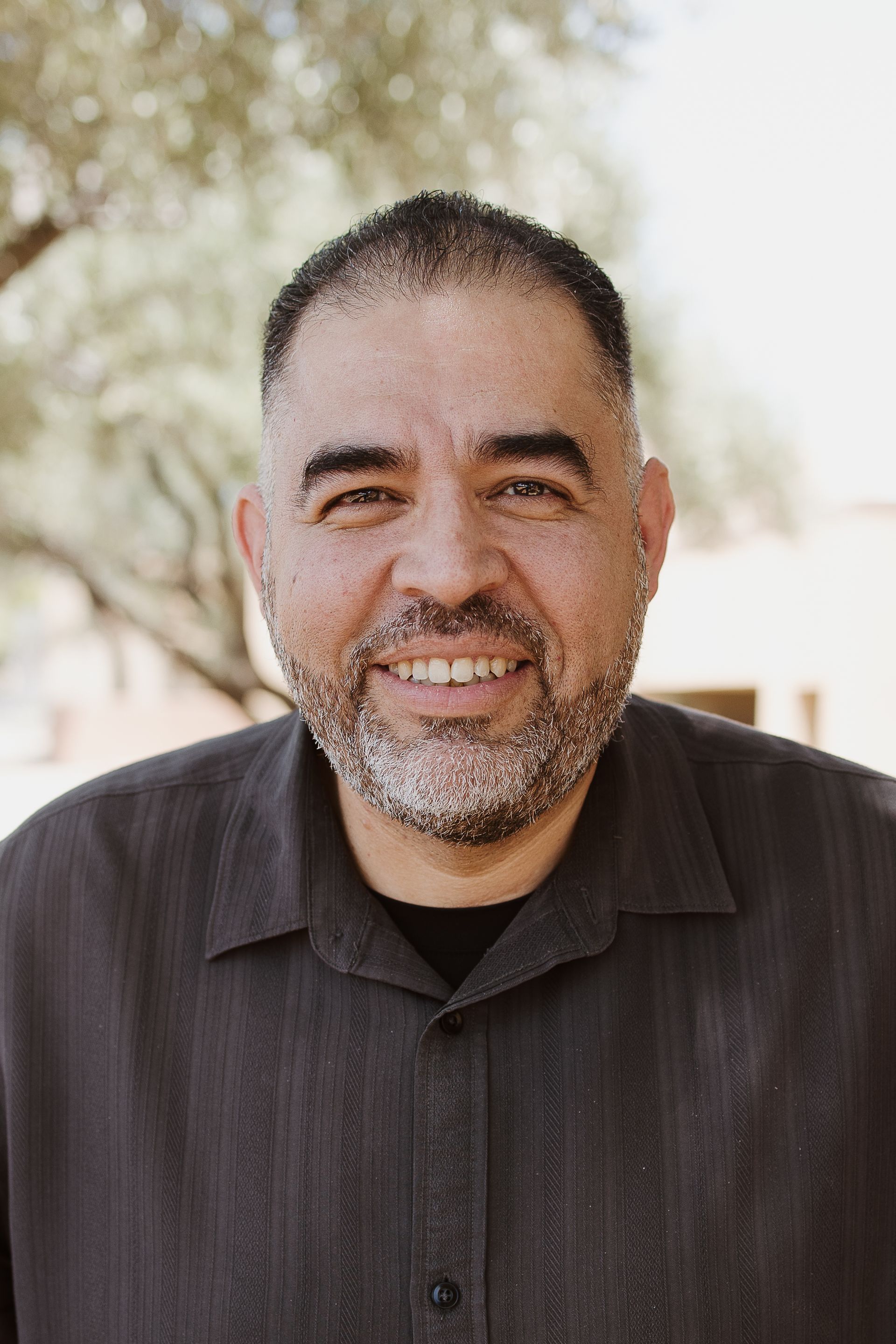 A man with a beard is smiling for the camera while wearing a black shirt.