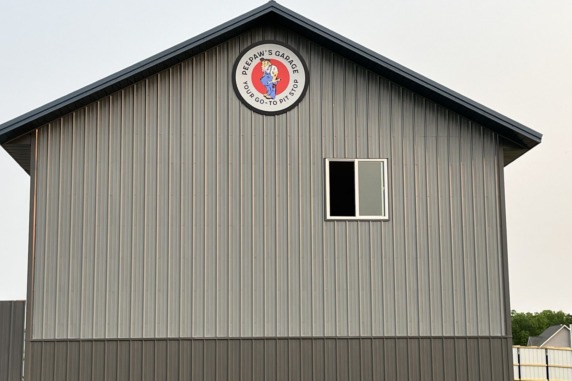 Gray and brown metal-sided building with a small window and a circular sign | PeePaw's Garage