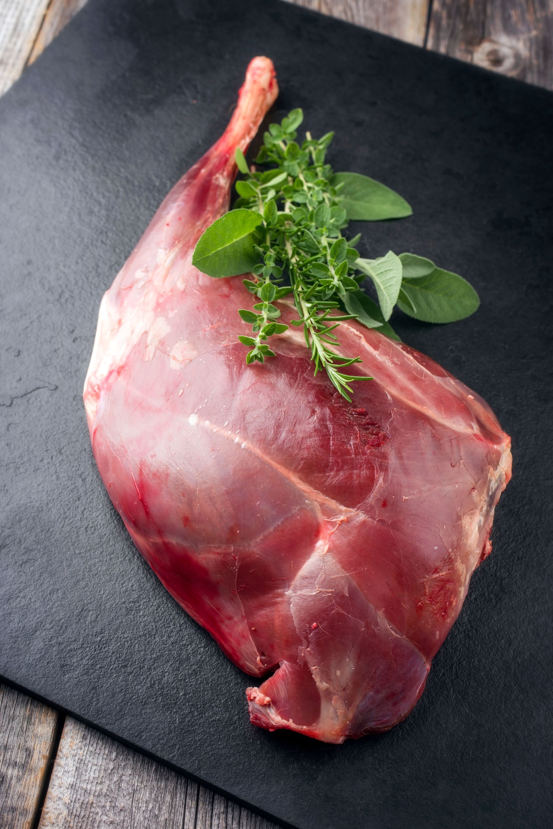 Rohe Rehkeule mit Kräutern auf schwarzem Untergrund.