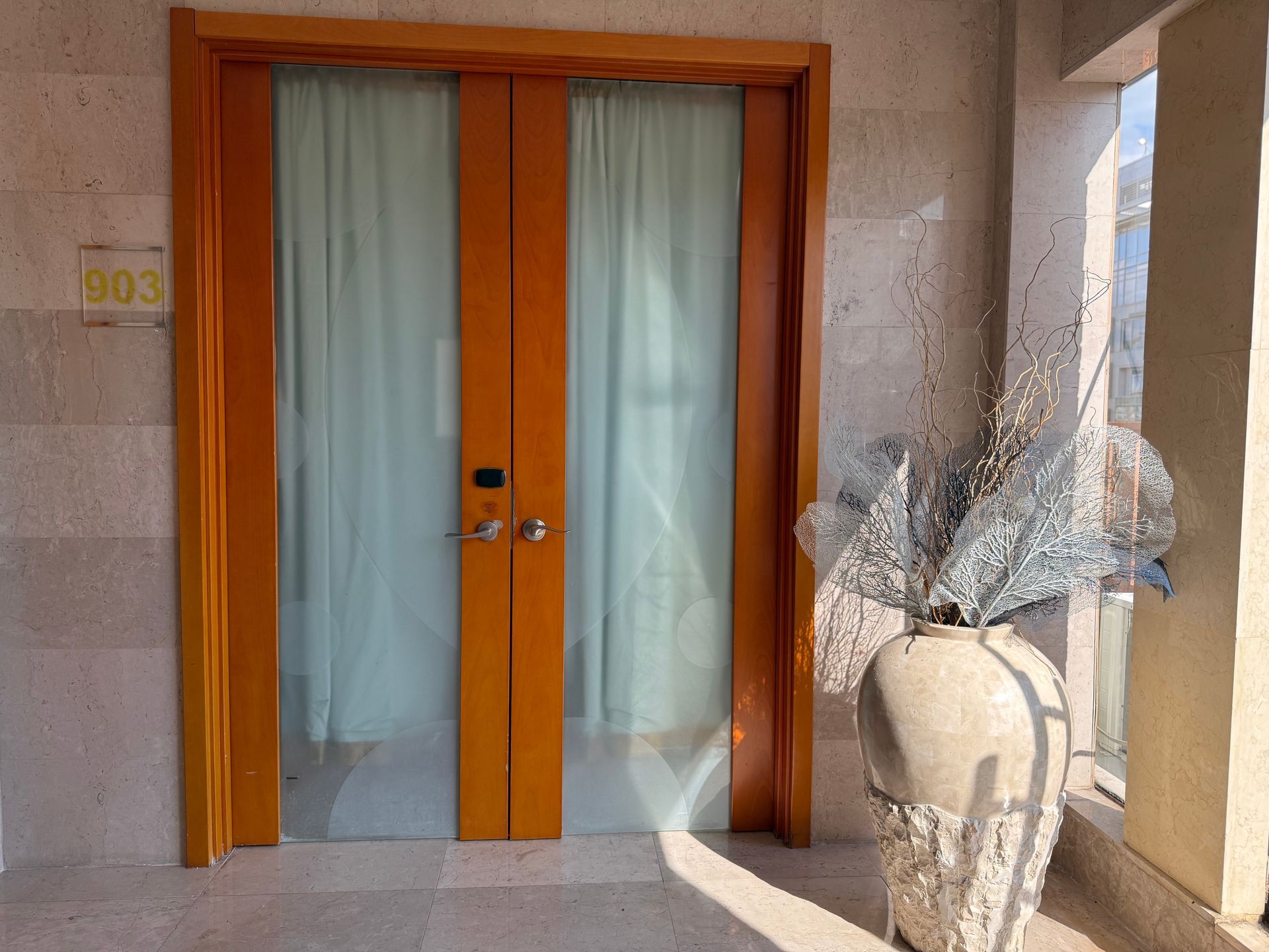 Wooden double doors with frosted glass, light blue curtains, and a decorative vase.