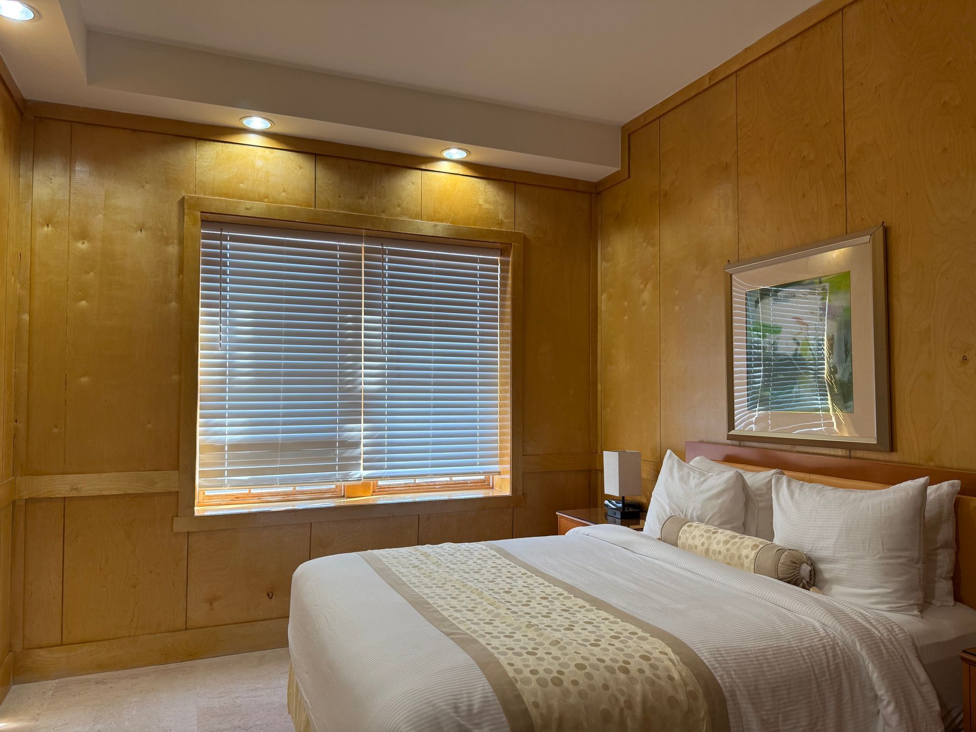 Bedroom with a bed, window, wooden paneling, and a framed picture.