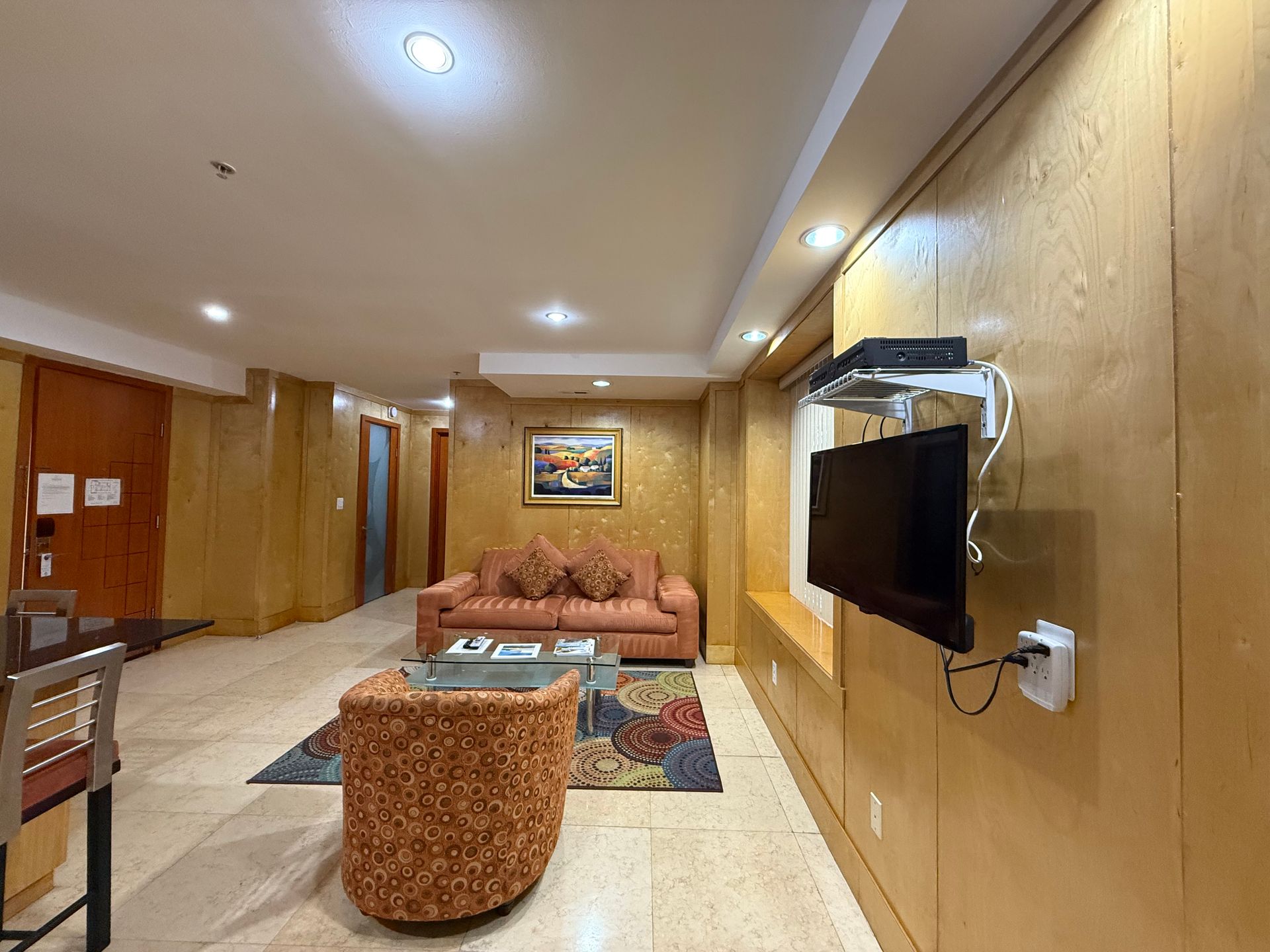 Living room with wood paneling, TV, couch, chair, rug, and painting.