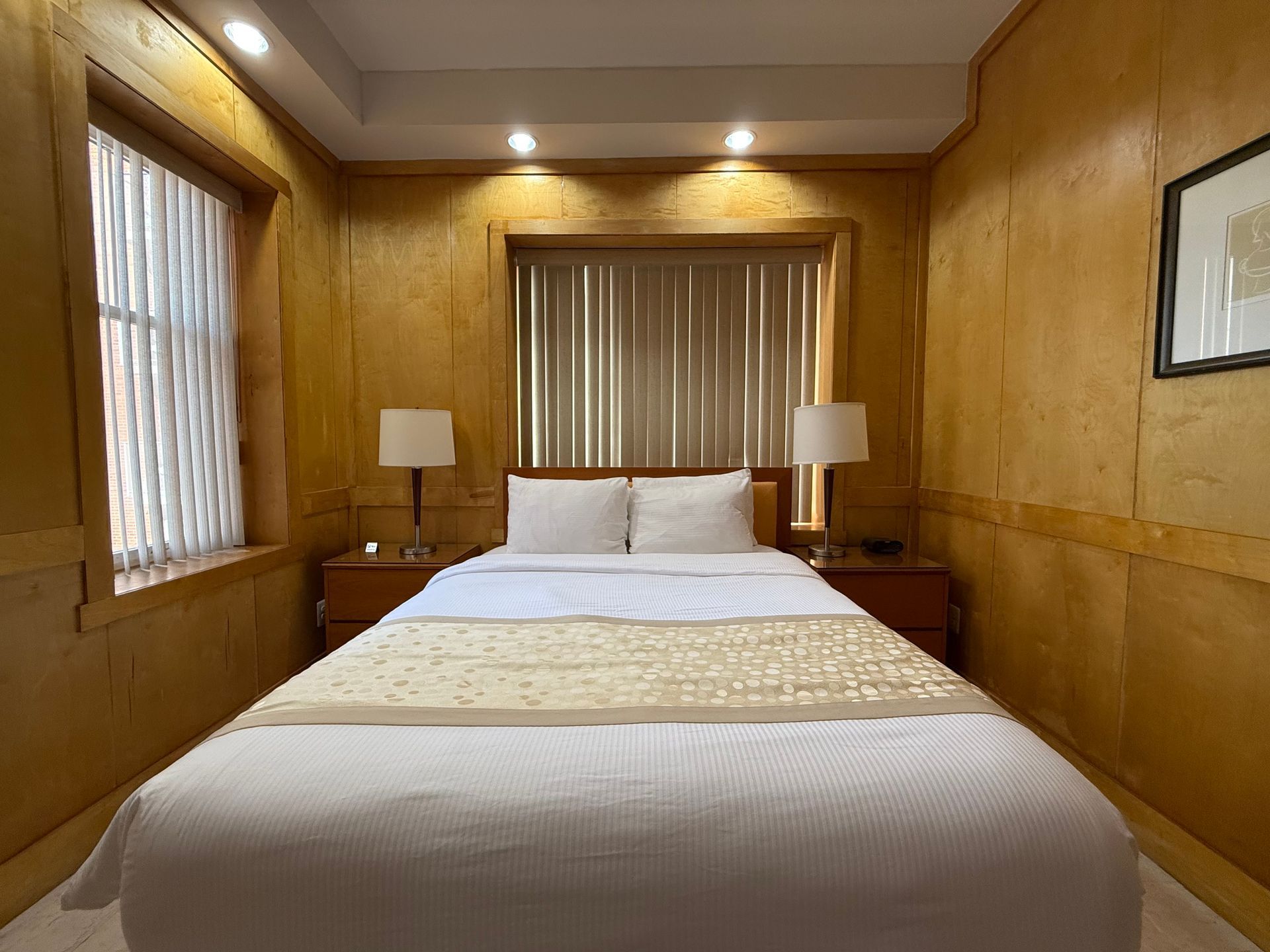 Bedroom with a double bed, nightstands, lamps, and a window with blinds. Walls are gold.