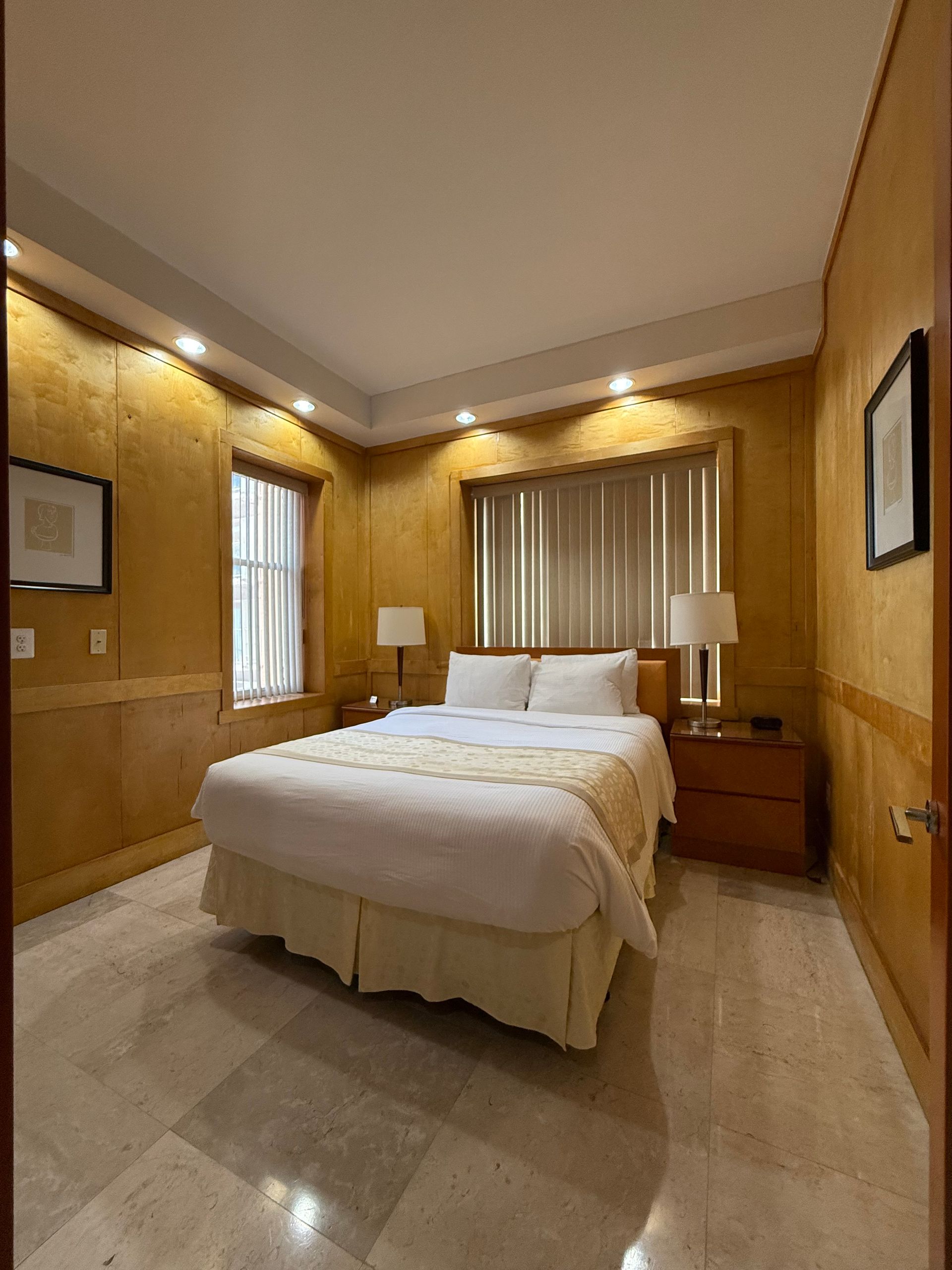 Bedroom with beige and gold walls, a bed, two nightstands, and a marble floor.