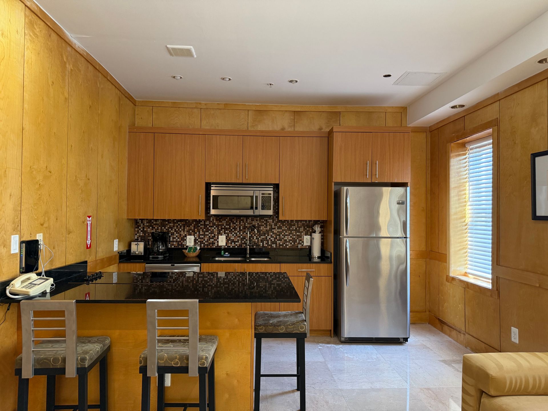 Kitchen with wood paneling, stainless steel appliances, breakfast bar, and stools.