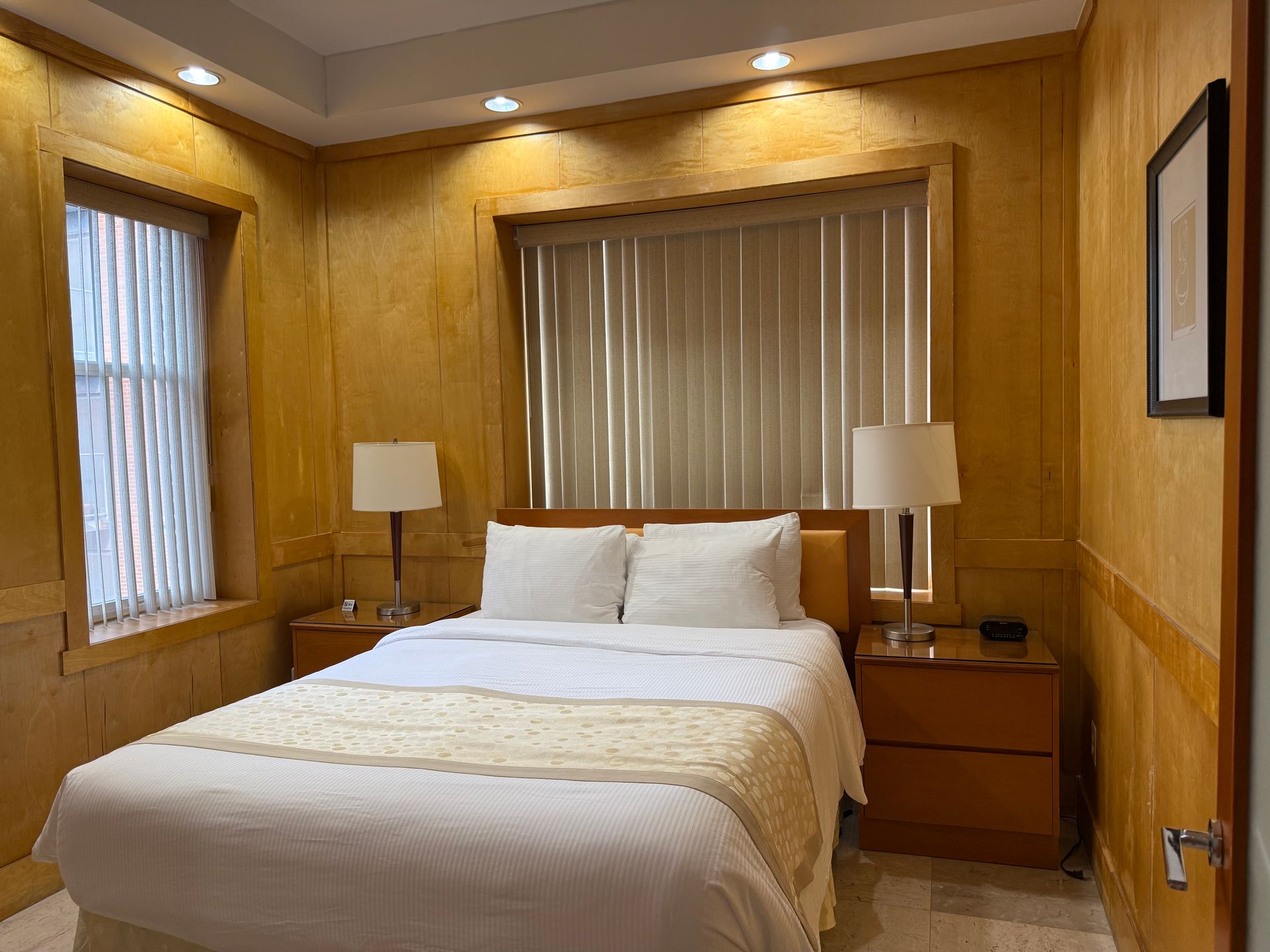 Bedroom with a double bed, nightstands, lamps, and a window with blinds. Yellow walls.