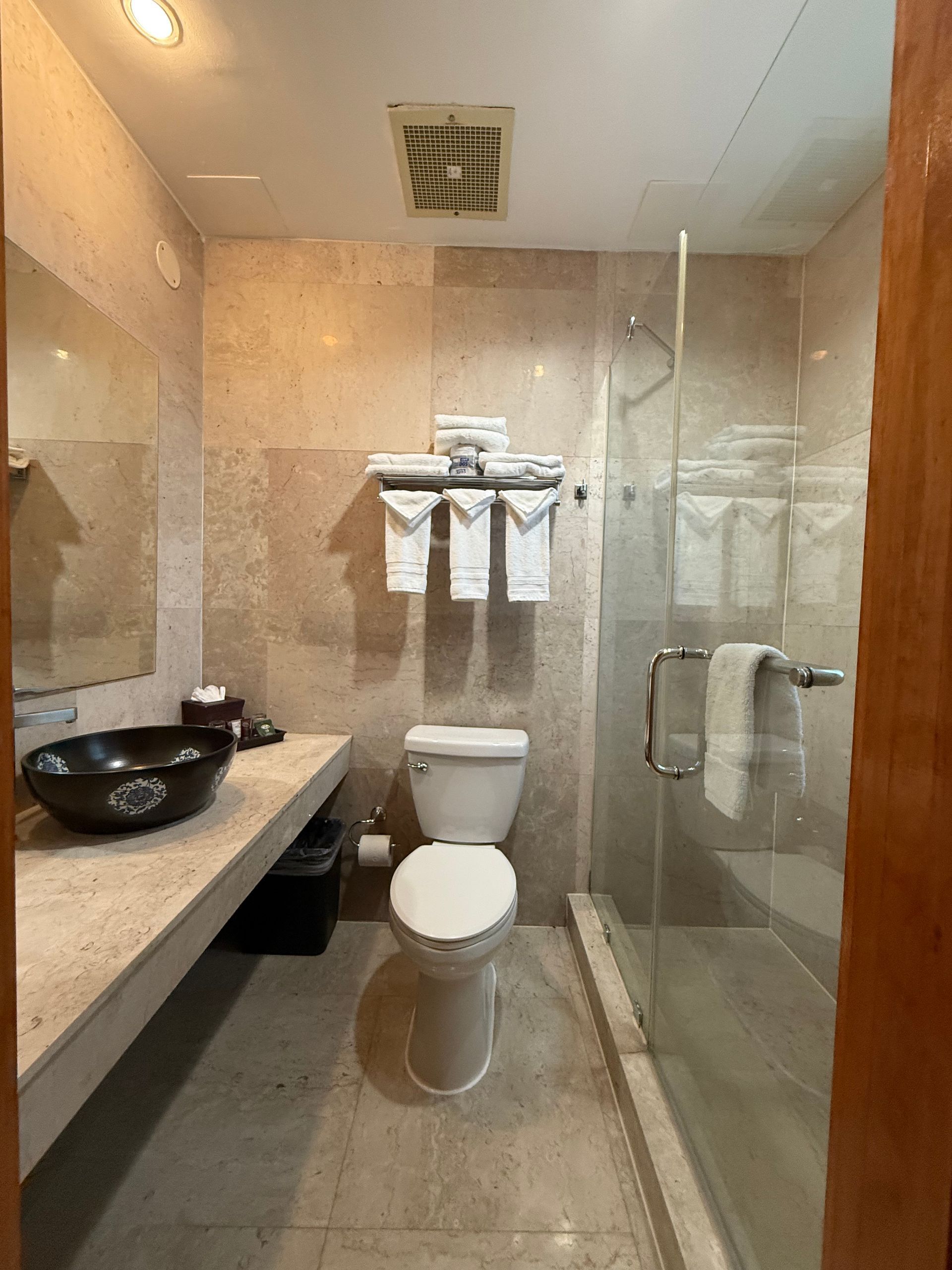 Bathroom with toilet, glass shower, stone tile, and dark vessel sink.