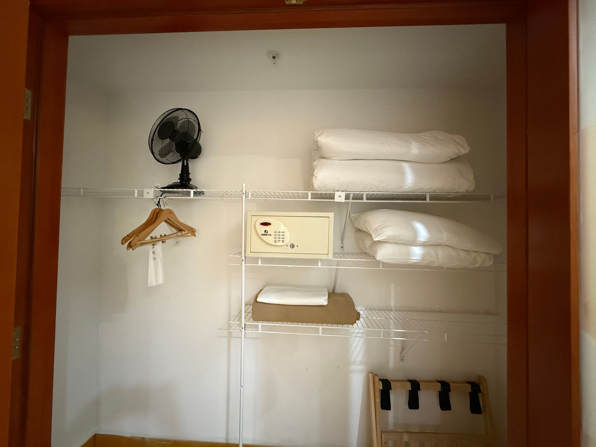 A closet with shelves. It has a fan, hangers, a safe, and folded blankets.