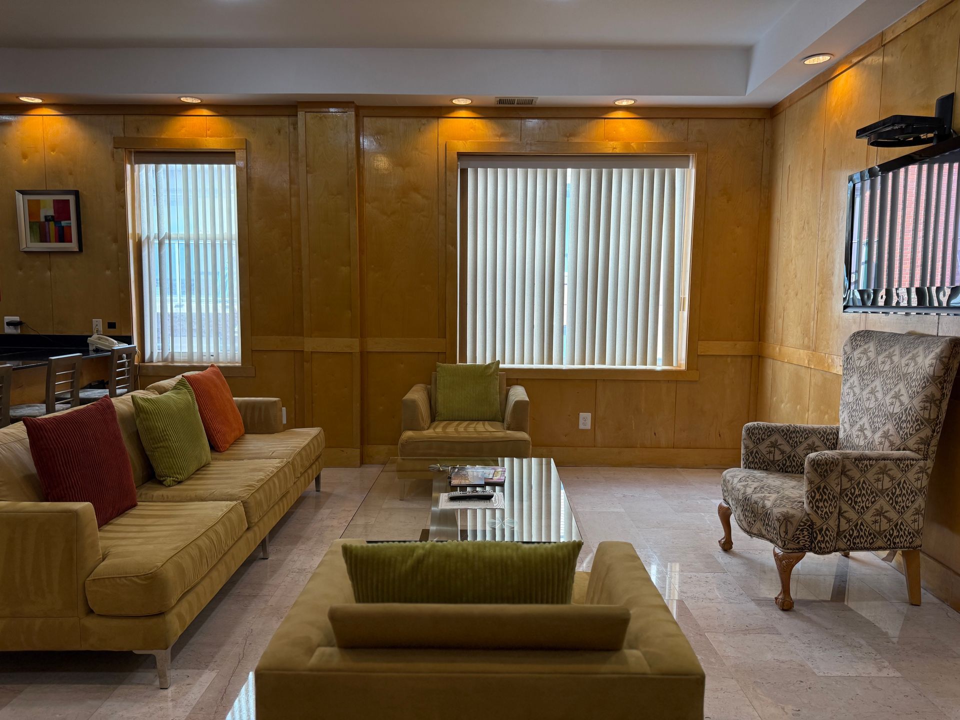 Cozy living room with yellow sofa, patterned armchairs, window, and wall-mounted TV.