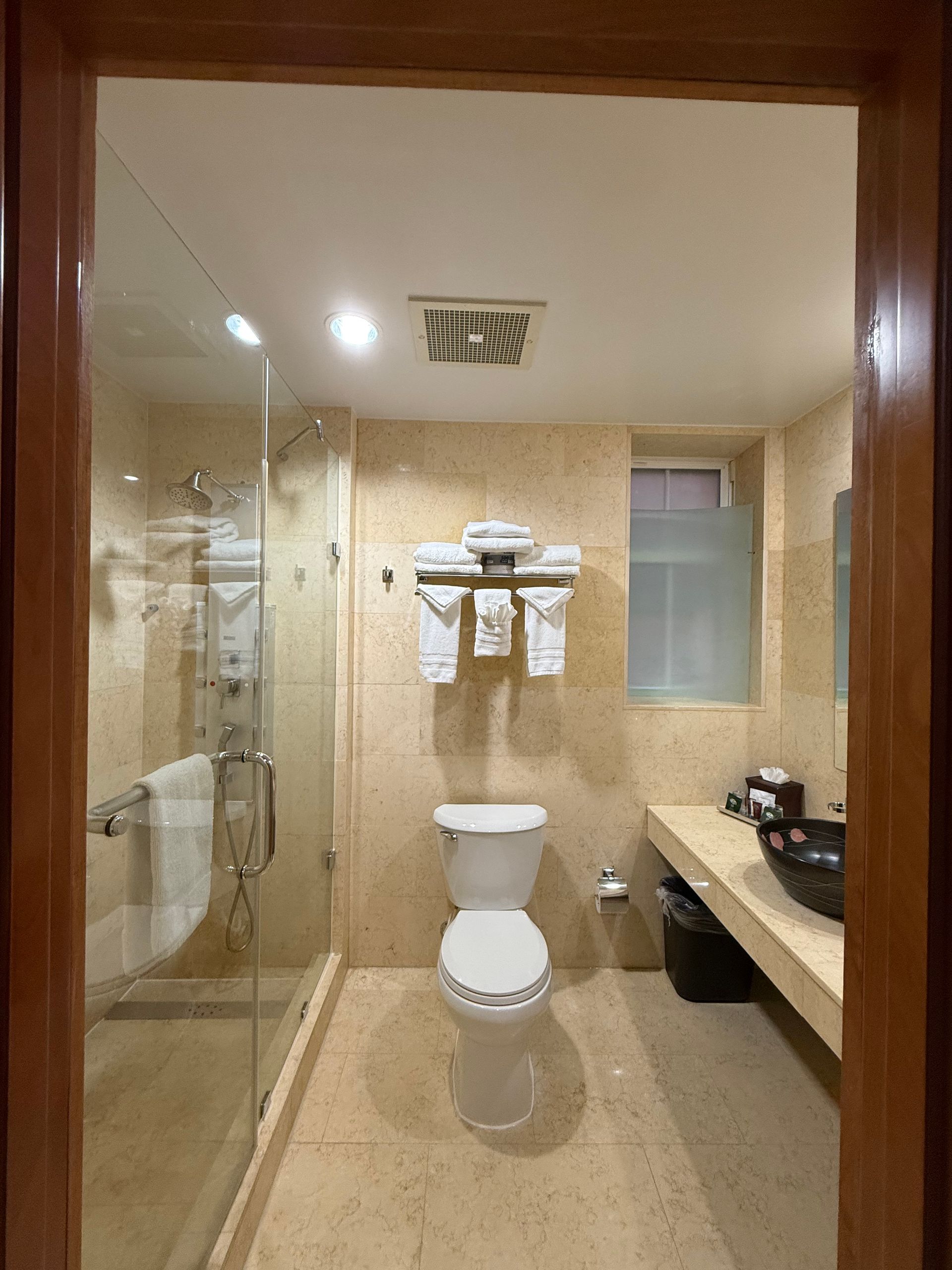 Bathroom interior with toilet, shower, sink, and towels; tan walls and tile.