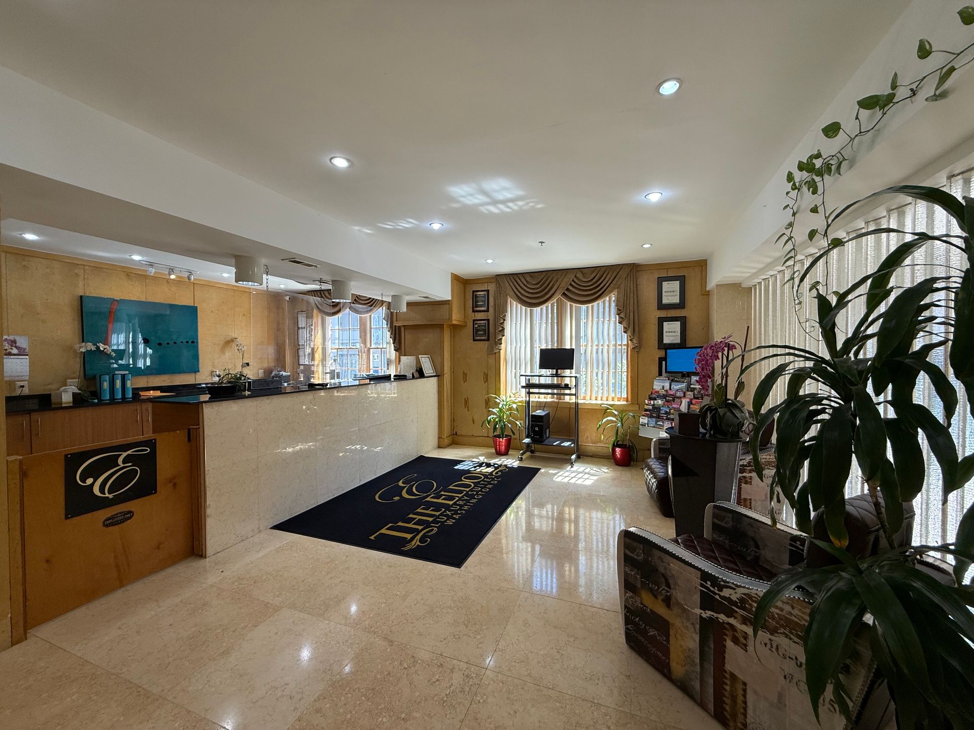 Reception area with counter, logo, rug, computer, and plants.