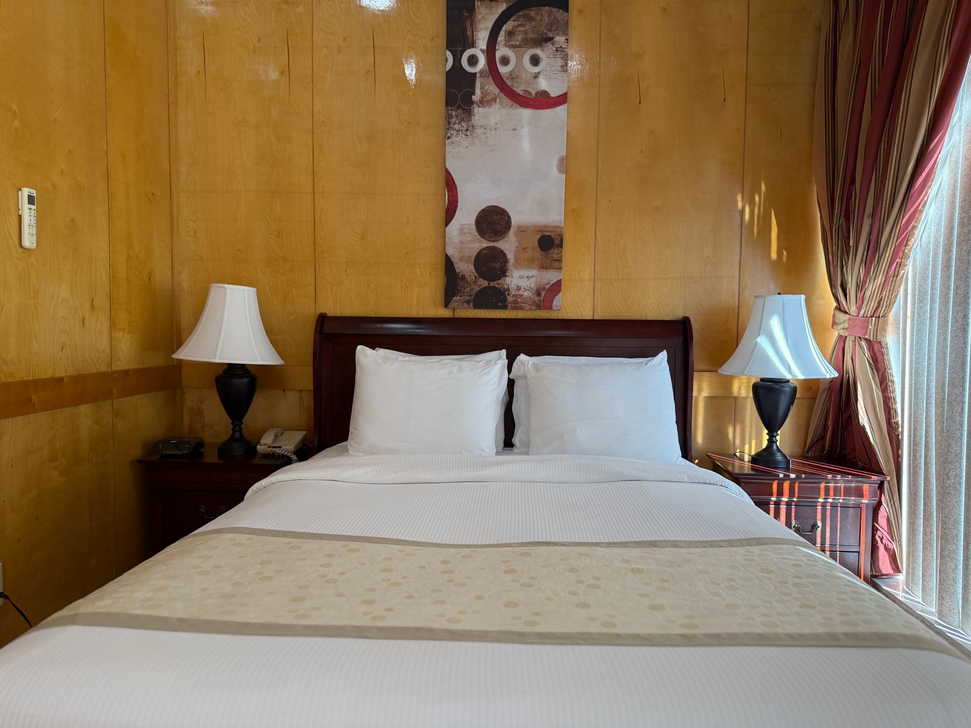 Bedroom with a bed, lamps, and art on the wall. Yellow walls, curtains.