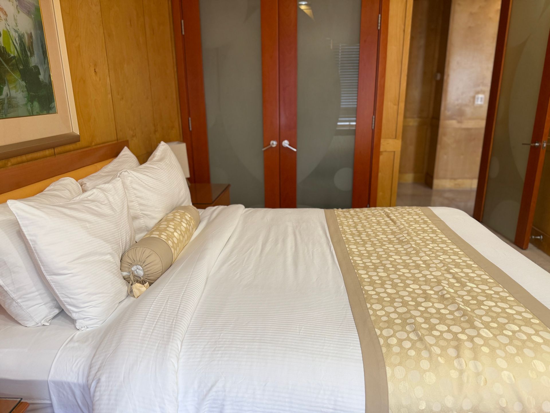 A bed with white bedding and a gold patterned runner, in a room with wood paneling.