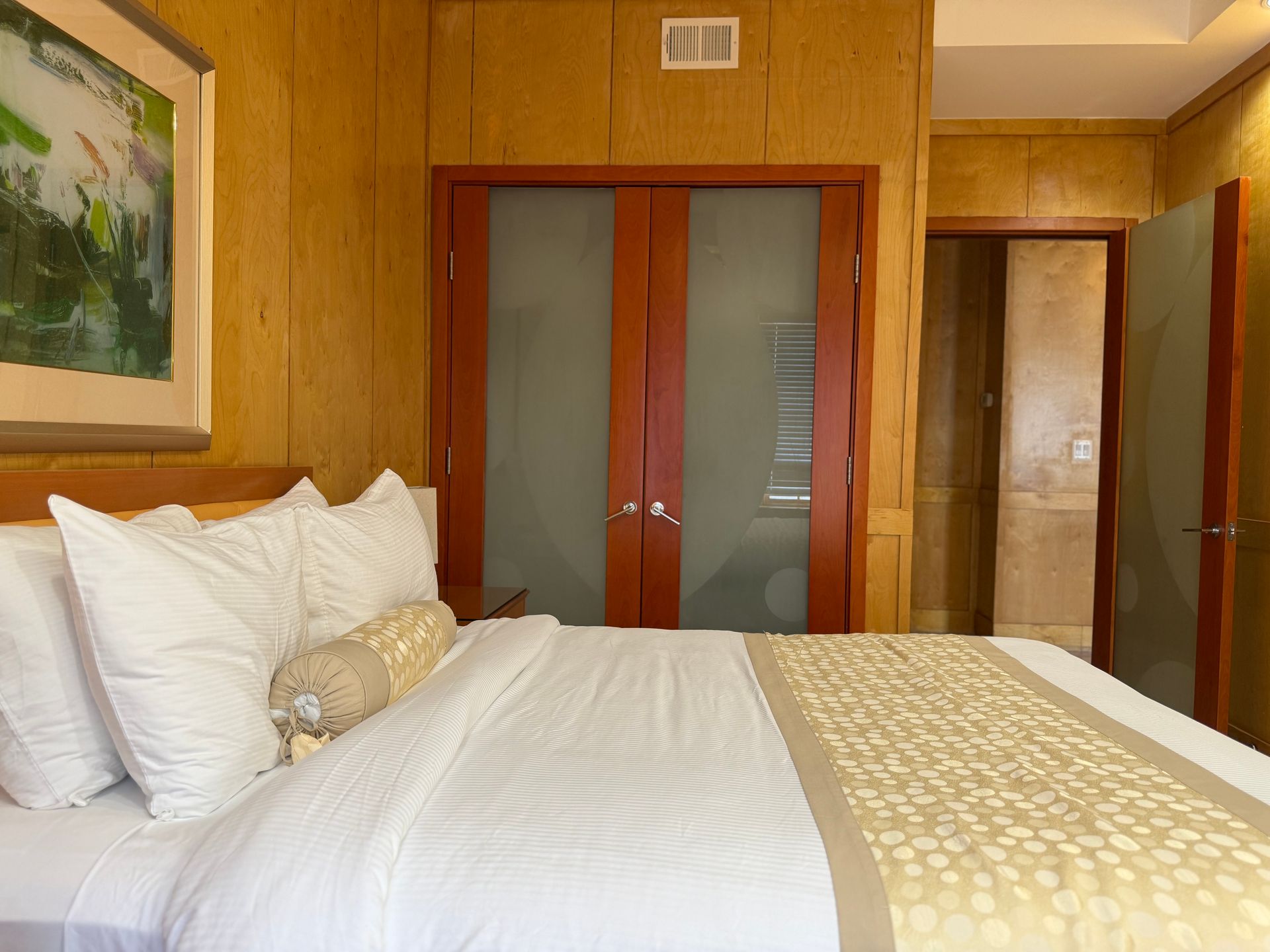 Bedroom with a bed, closed closet doors, and a partially visible bathroom. Wooden paneling.