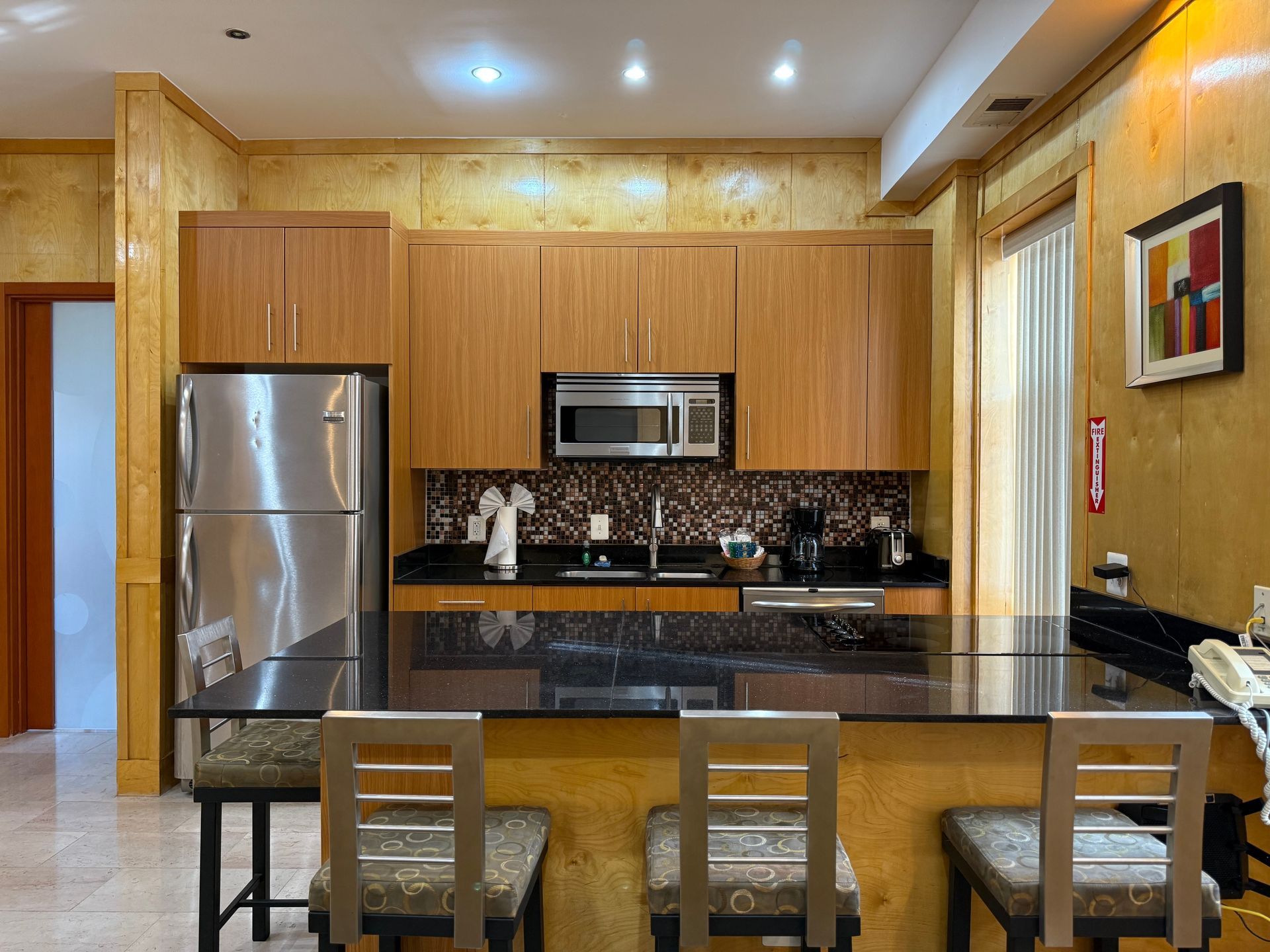 Kitchen with stainless steel refrigerator, wooden cabinets, and granite countertops; three bar stools in front of the island.