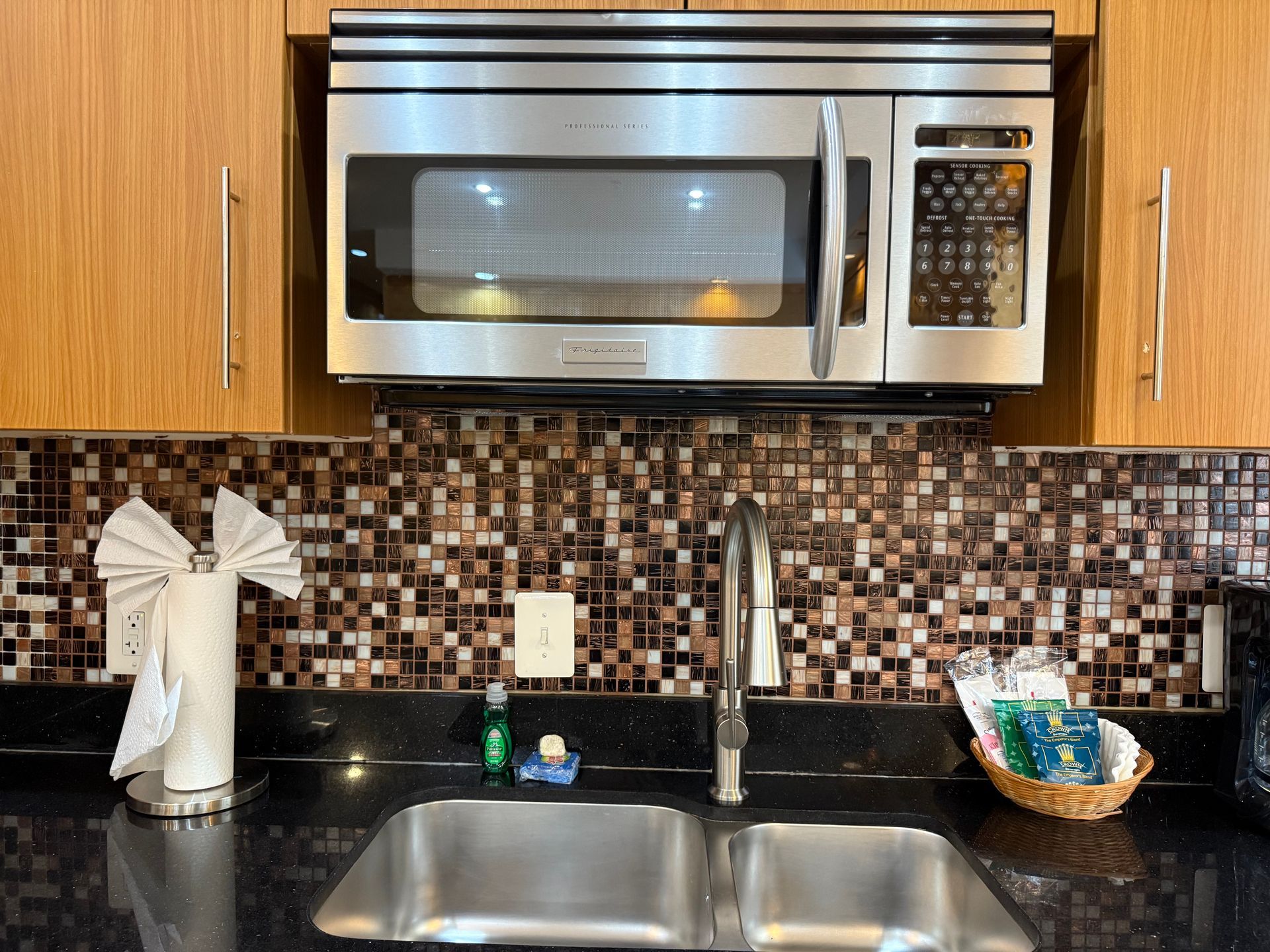 Kitchen sink with microwave above, black countertop, and tiled backsplash.