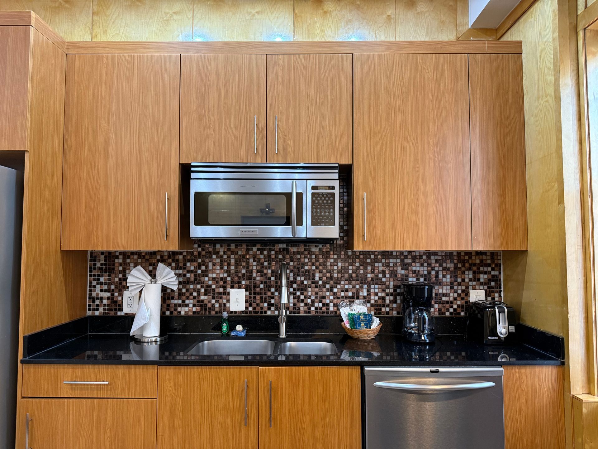 Kitchen with wood cabinets, microwave, black countertop, stainless steel sink, and appliances.