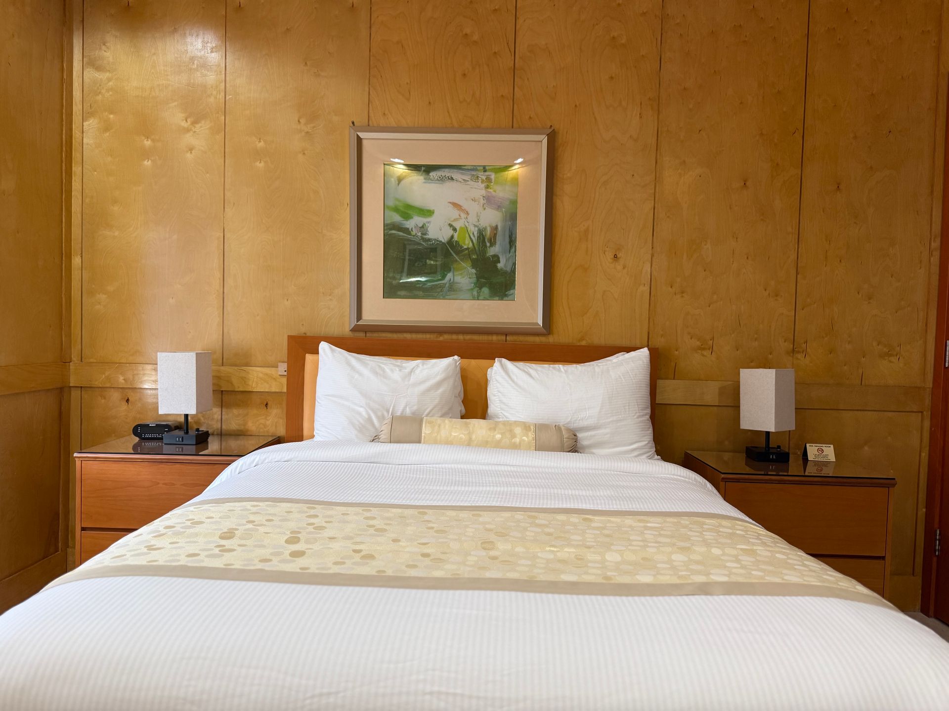 Bedroom with wooden paneling, a made bed, nightstands with lamps, and artwork.