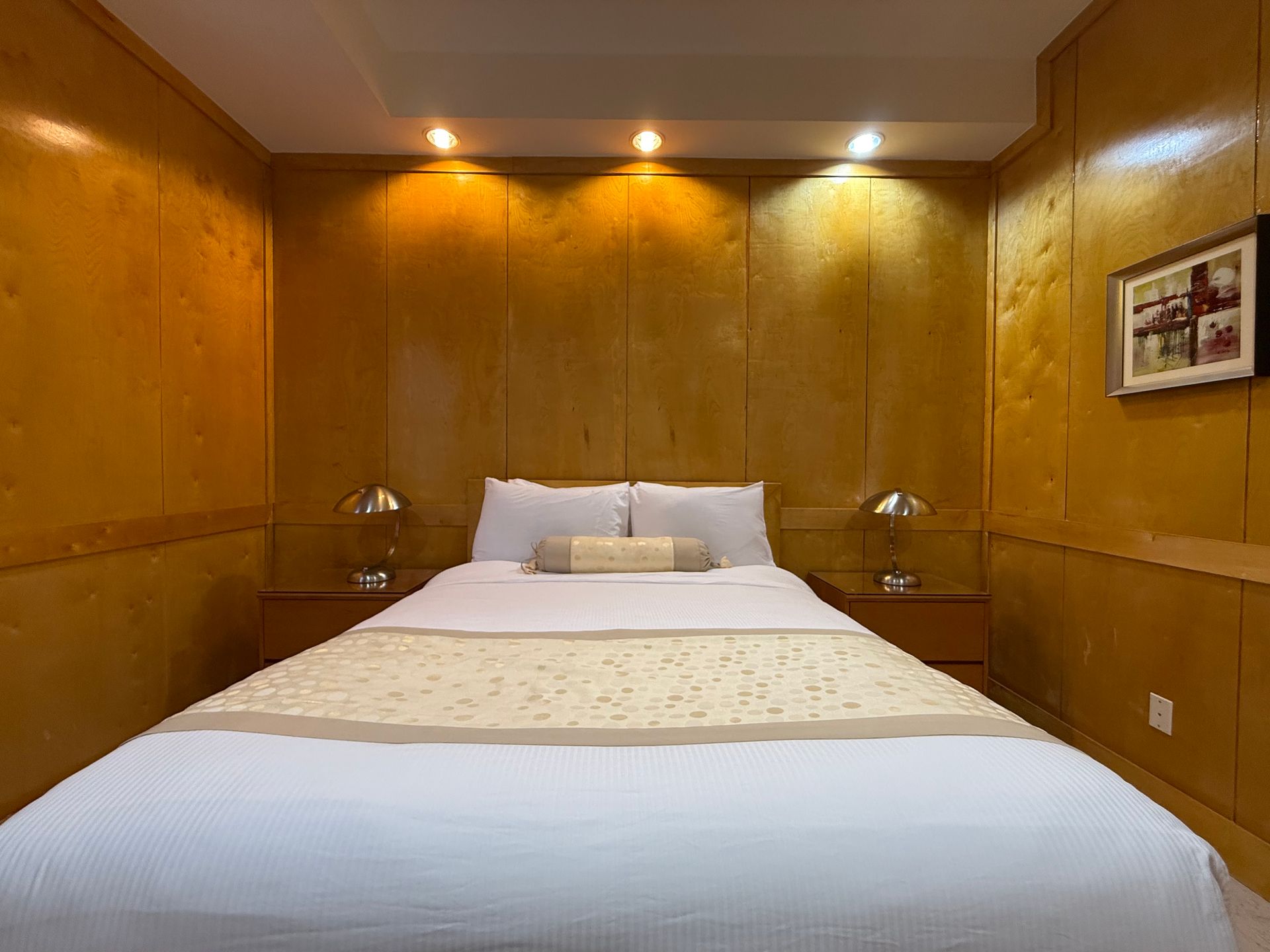 Cozy bedroom with wooden paneling, a bed with white and cream bedding, and bedside lamps.