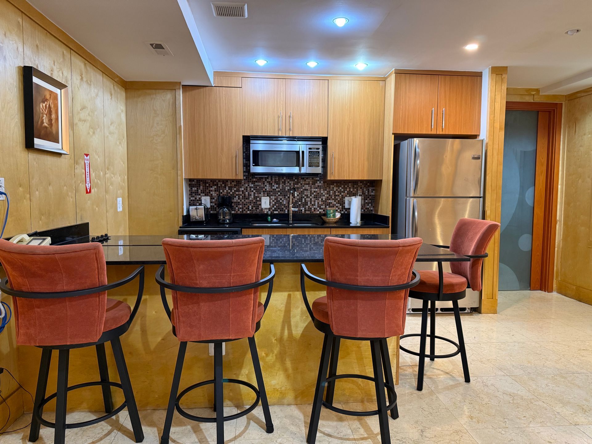A kitchen with bar seating, wooden cabinets, and stainless steel refrigerator.
