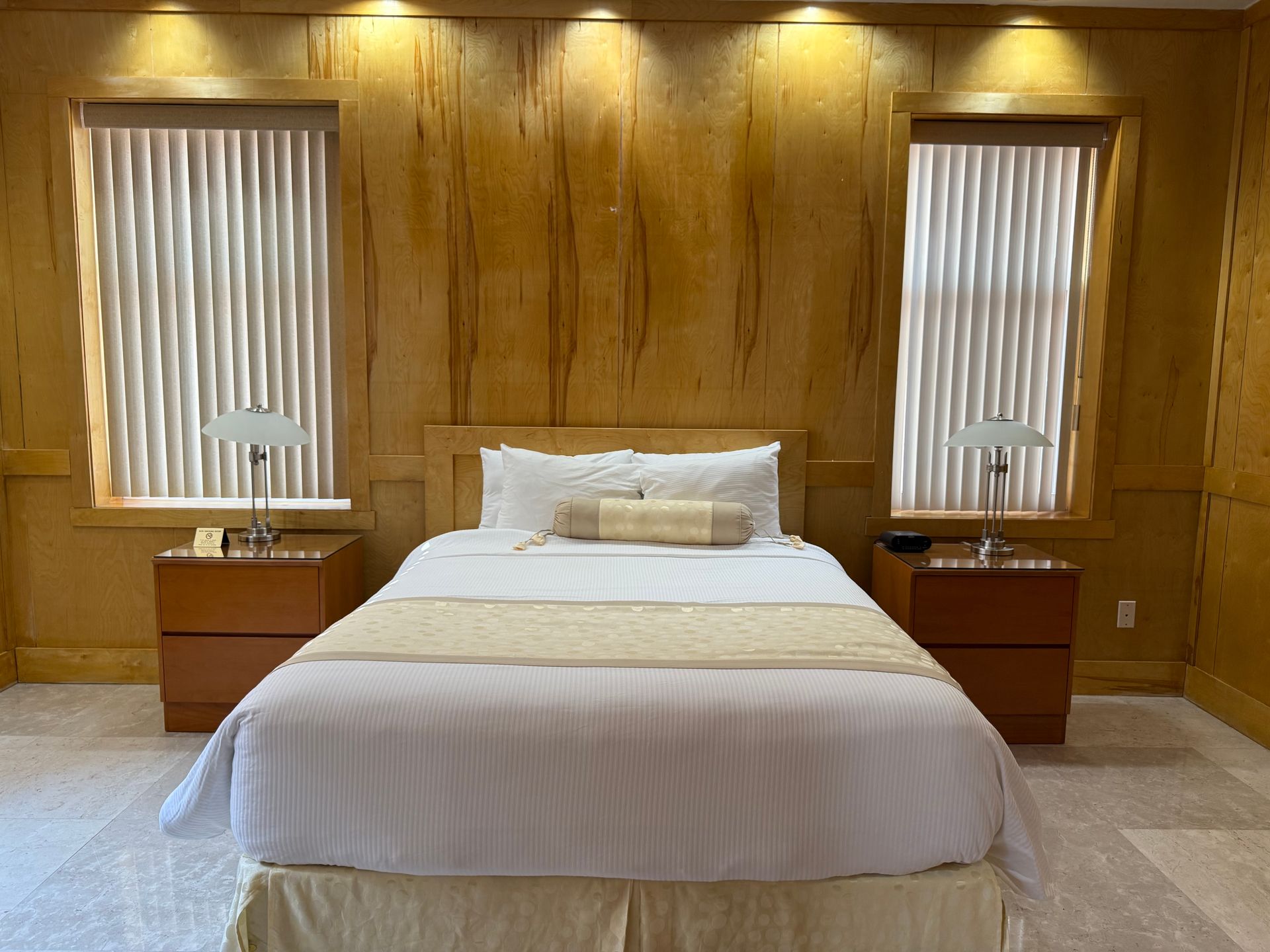Bedroom with a bed, two nightstands, two windows with blinds, and wood paneling.