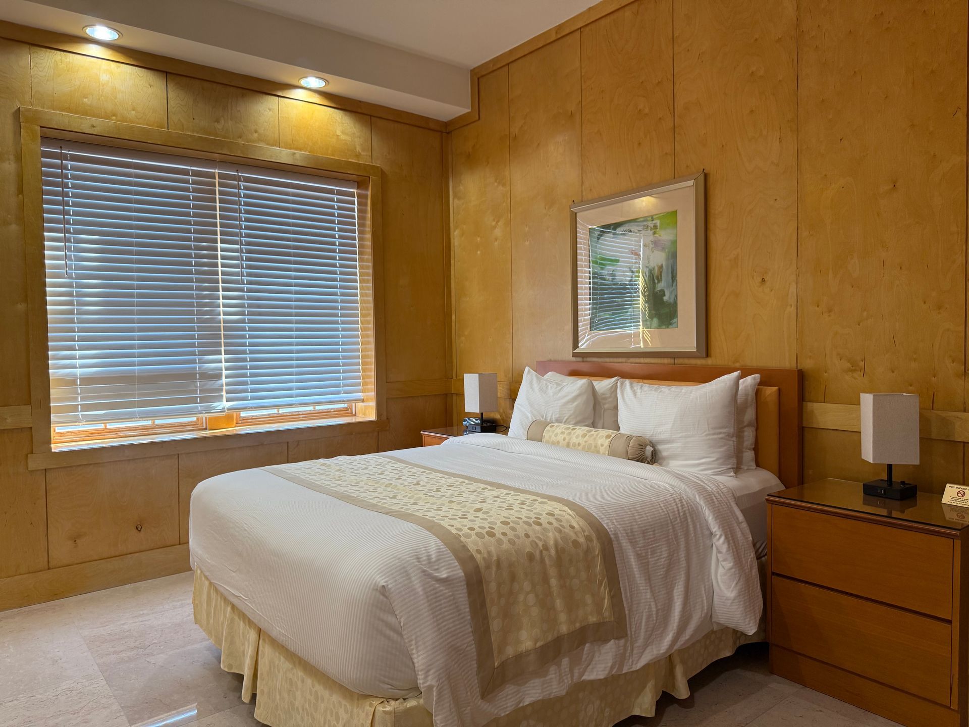 Bedroom with a bed, nightstands, and a window with blinds. Wood paneling covers the walls.