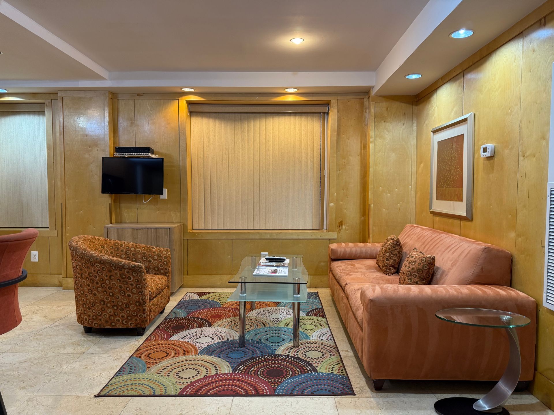 Living room with orange couch and patterned rug, centered on window with cream curtains.