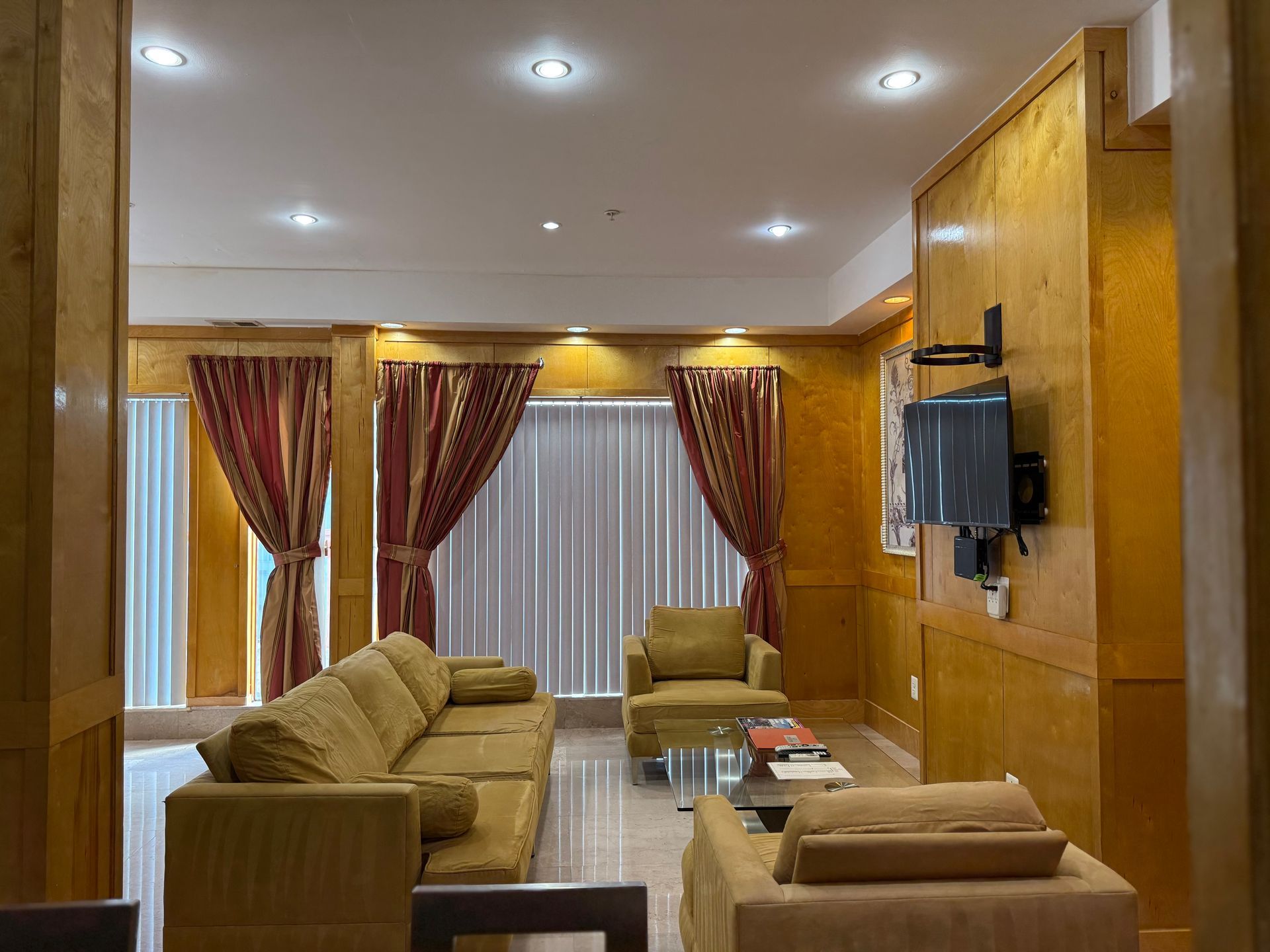 Living room with brown sofa, armchair, and curtains; TV mounted on wall.