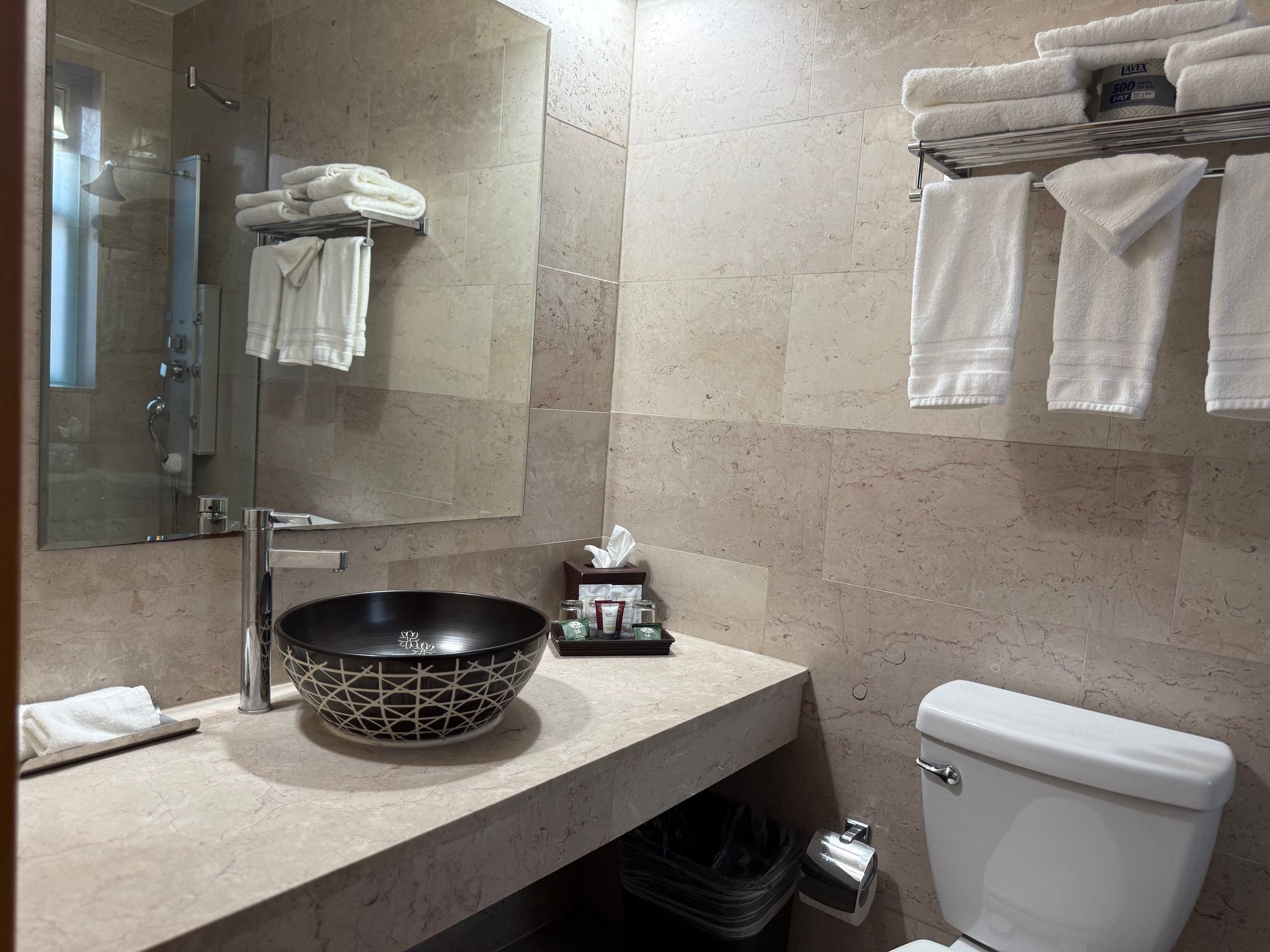 Bathroom with a decorative sink, towels, mirror, and toilet. Beige tile walls.