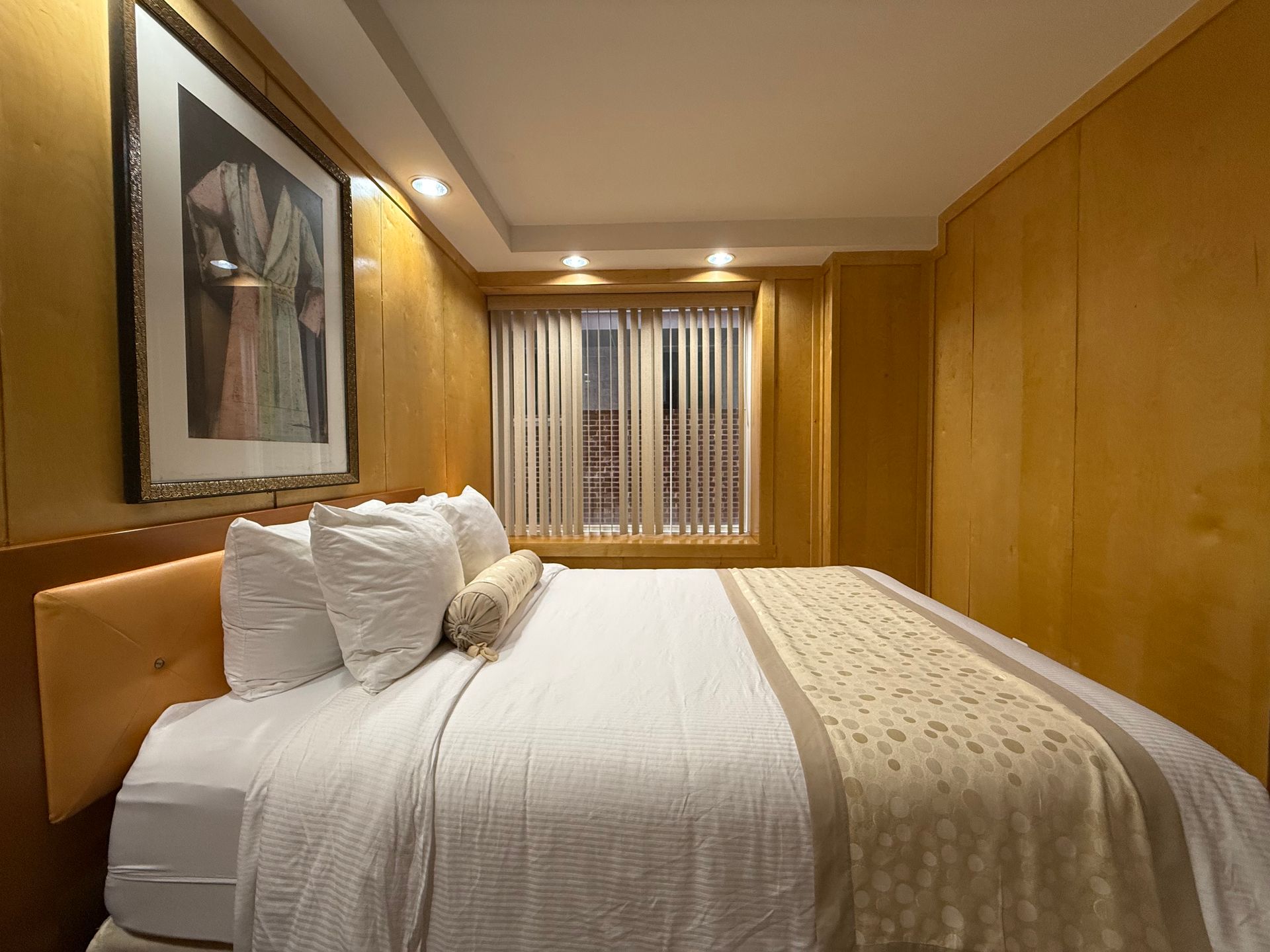 Bedroom with a bed, artwork, and window with blinds. Walls are wood-paneled.