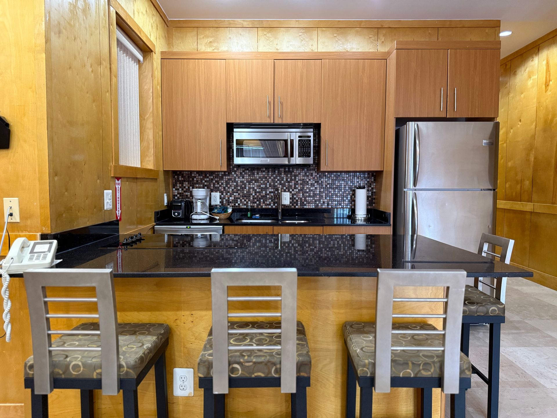 Small kitchen with wood cabinets, stainless steel appliances, and a breakfast bar with three stools.