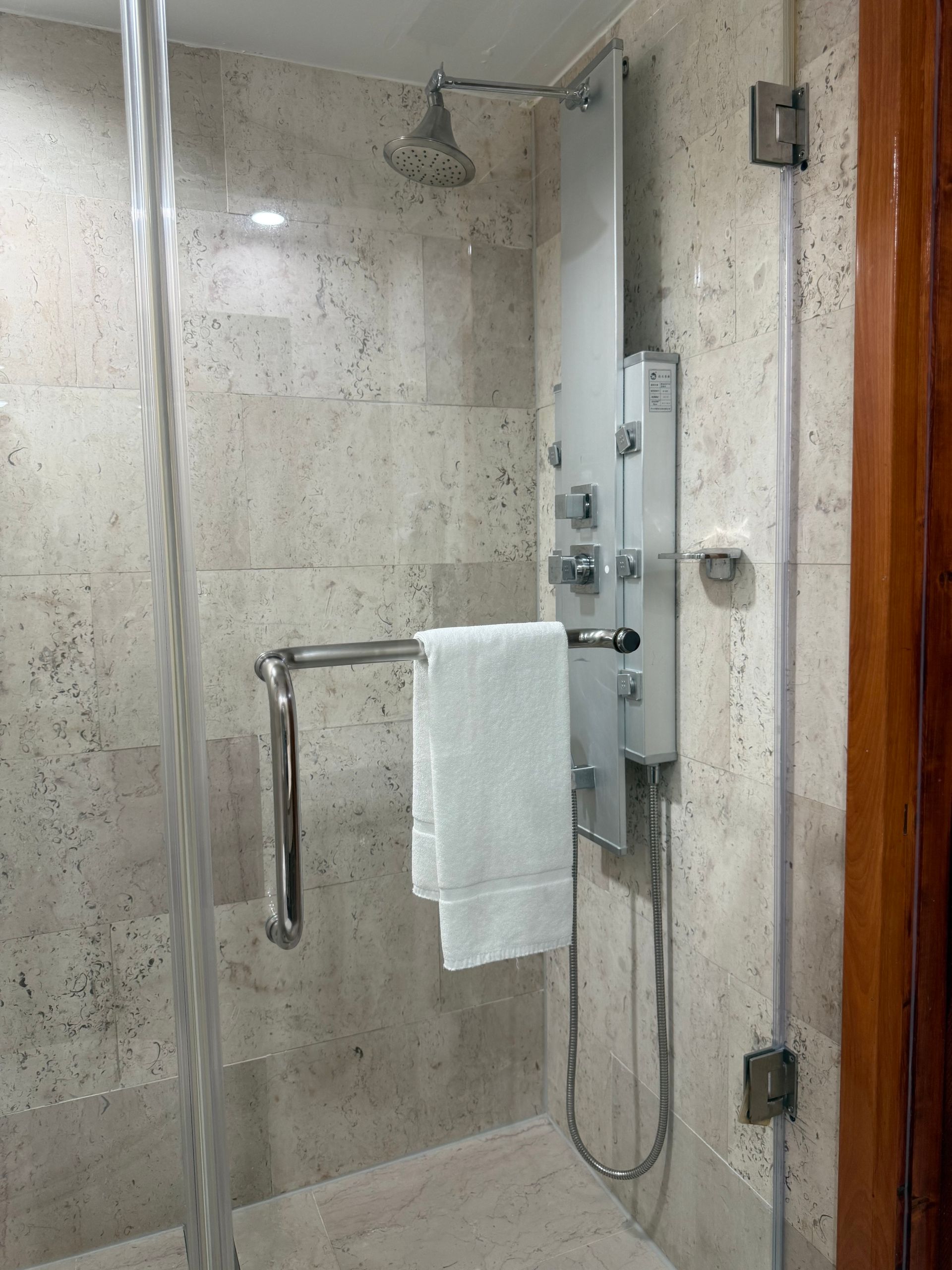 Shower stall with glass doors, silver fixtures, a white towel, and stone-look tiles.