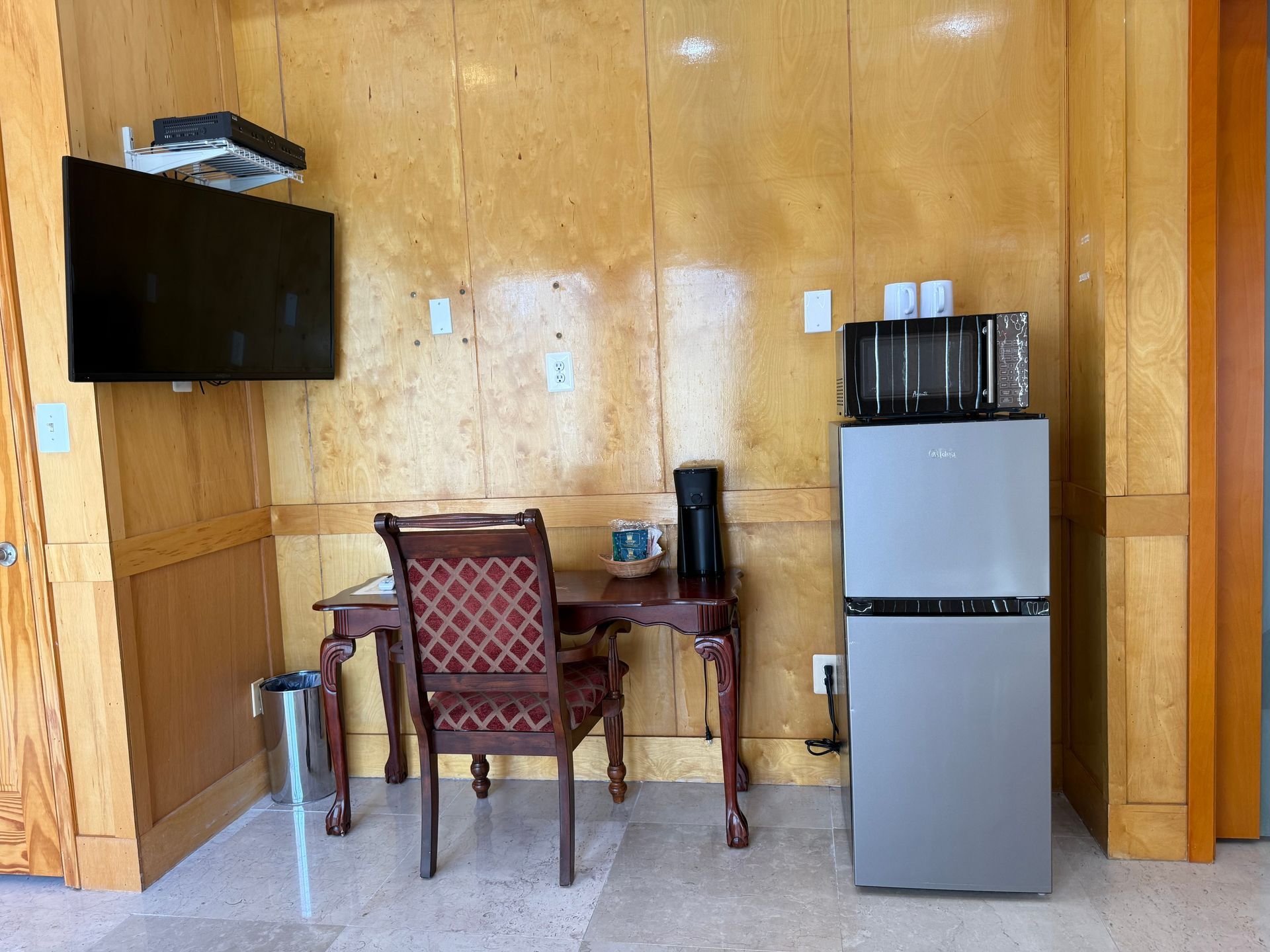 Small room with desk, TV, refrigerator, and microwave against wood-paneled wall.