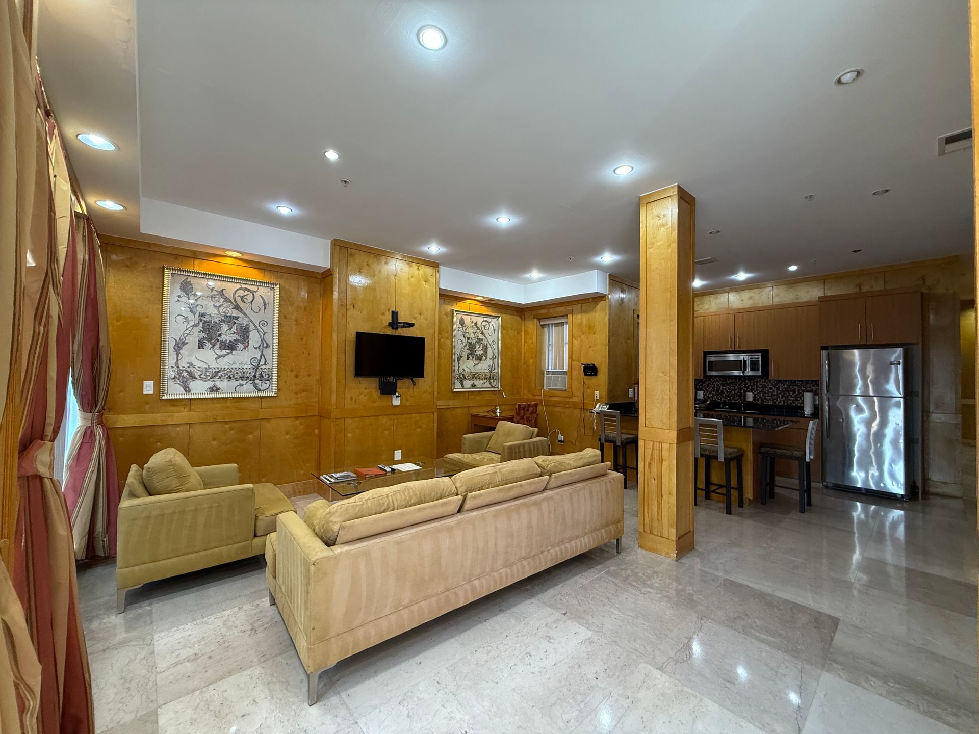 Living room with tan furniture, art, and a small kitchen area.