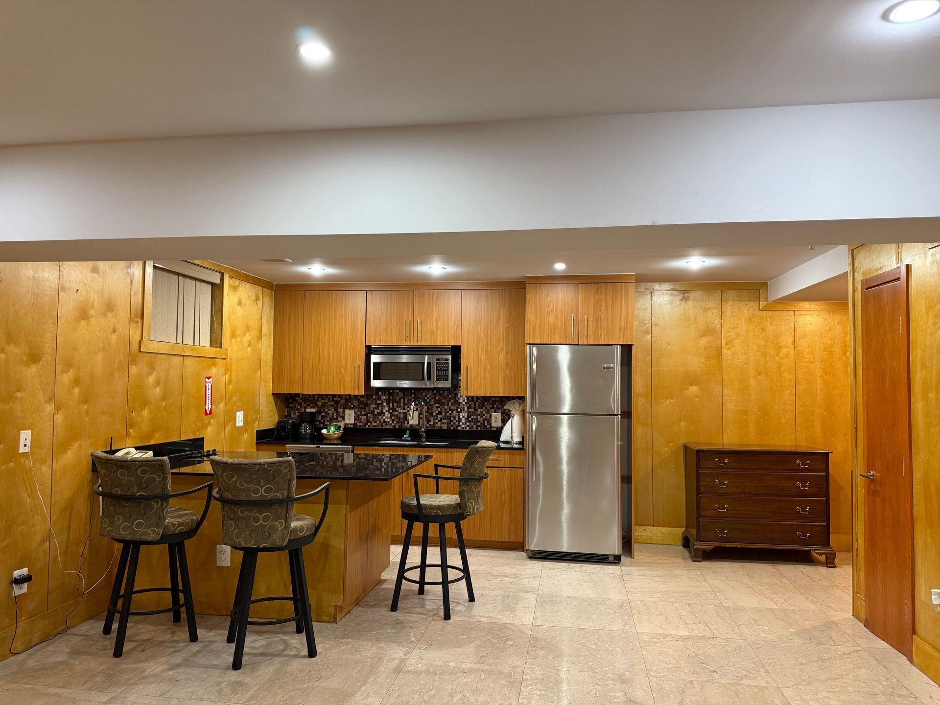 Kitchen with wood paneling, countertops, stainless steel refrigerator, and bar stools.