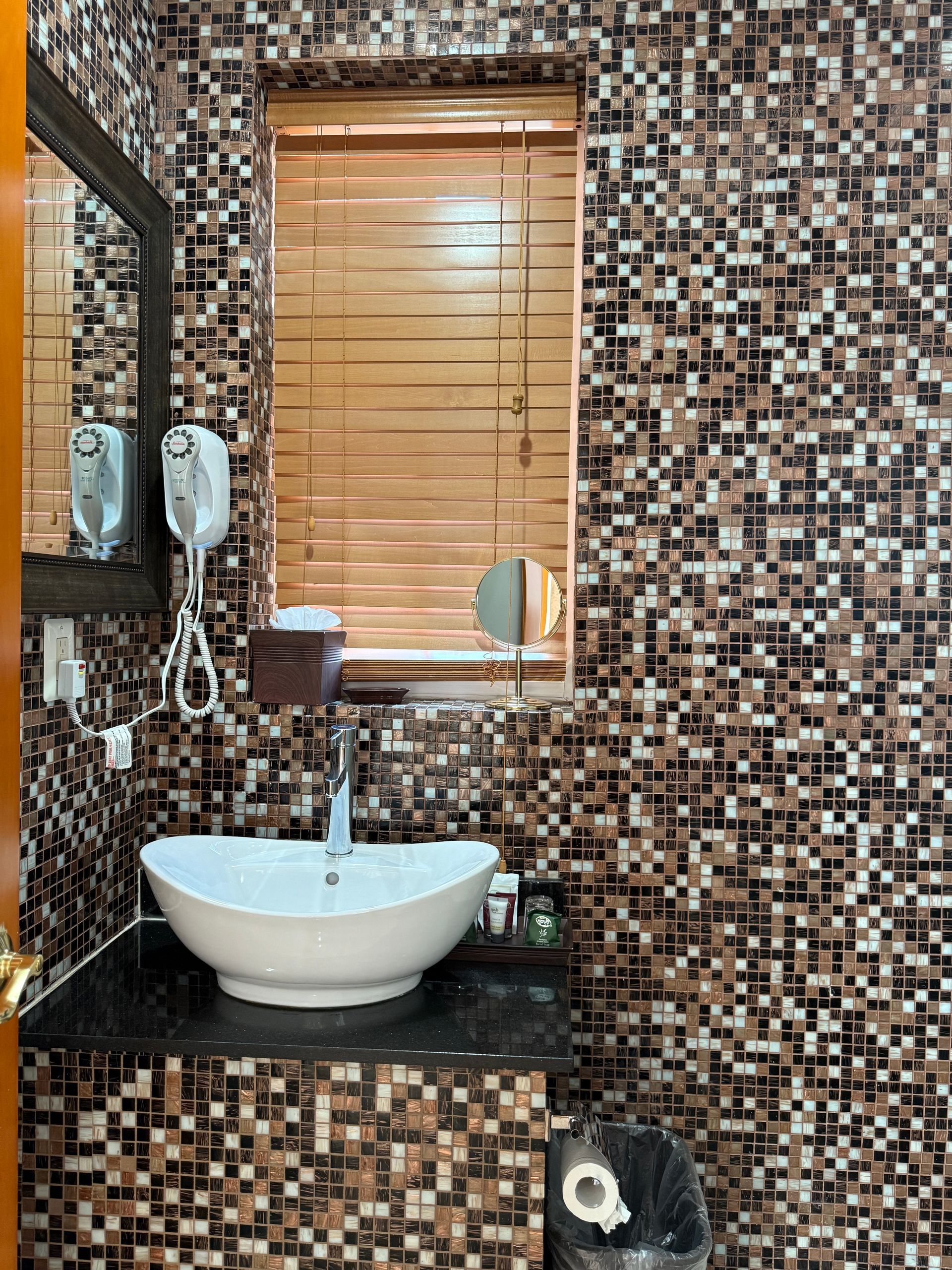 Bathroom with mosaic-tiled walls, a white sink, mirror, and a window with blinds.