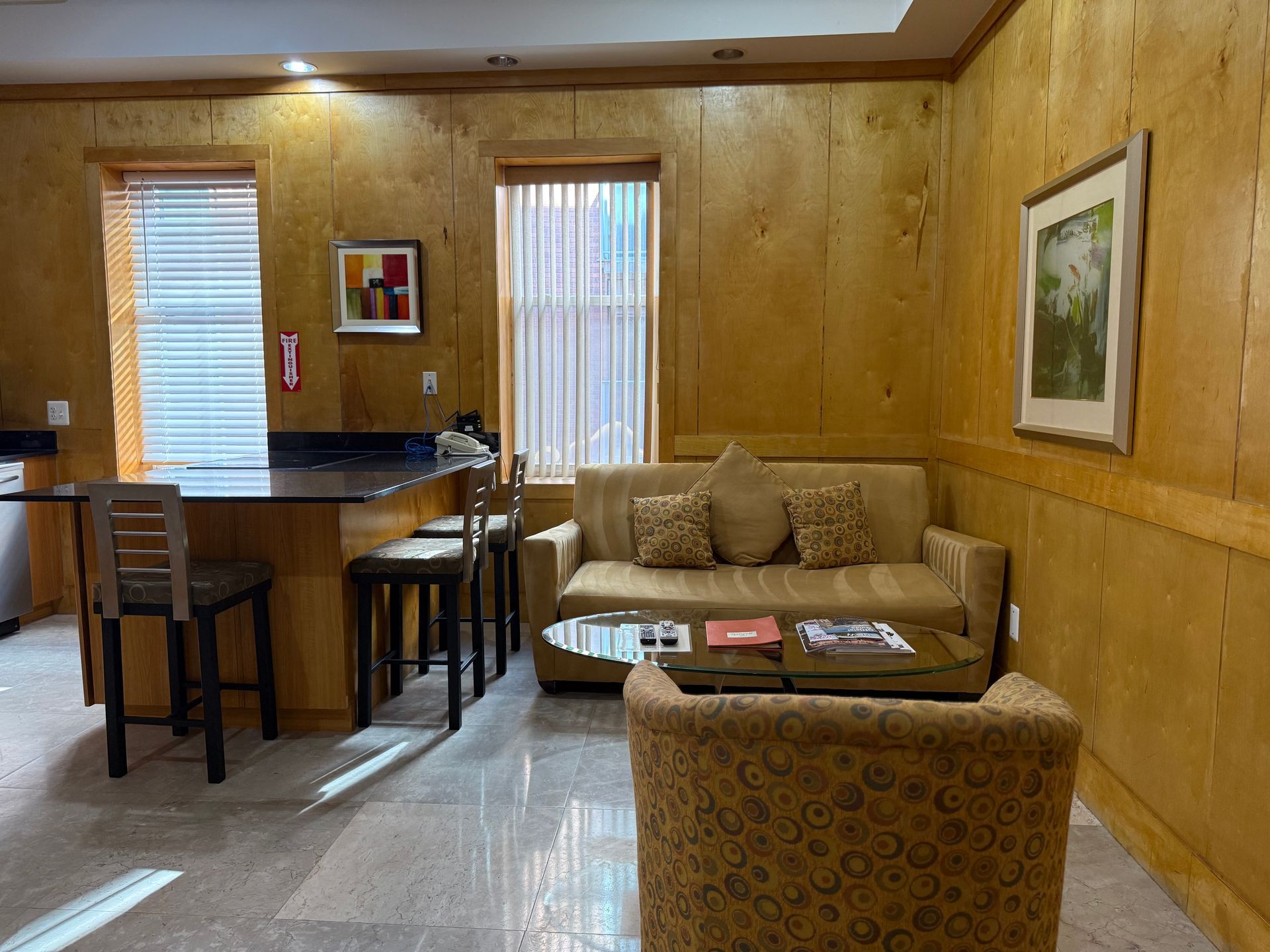 Living area with sofa, chairs, small table, and breakfast bar with two stools. Wooden walls and flooring.