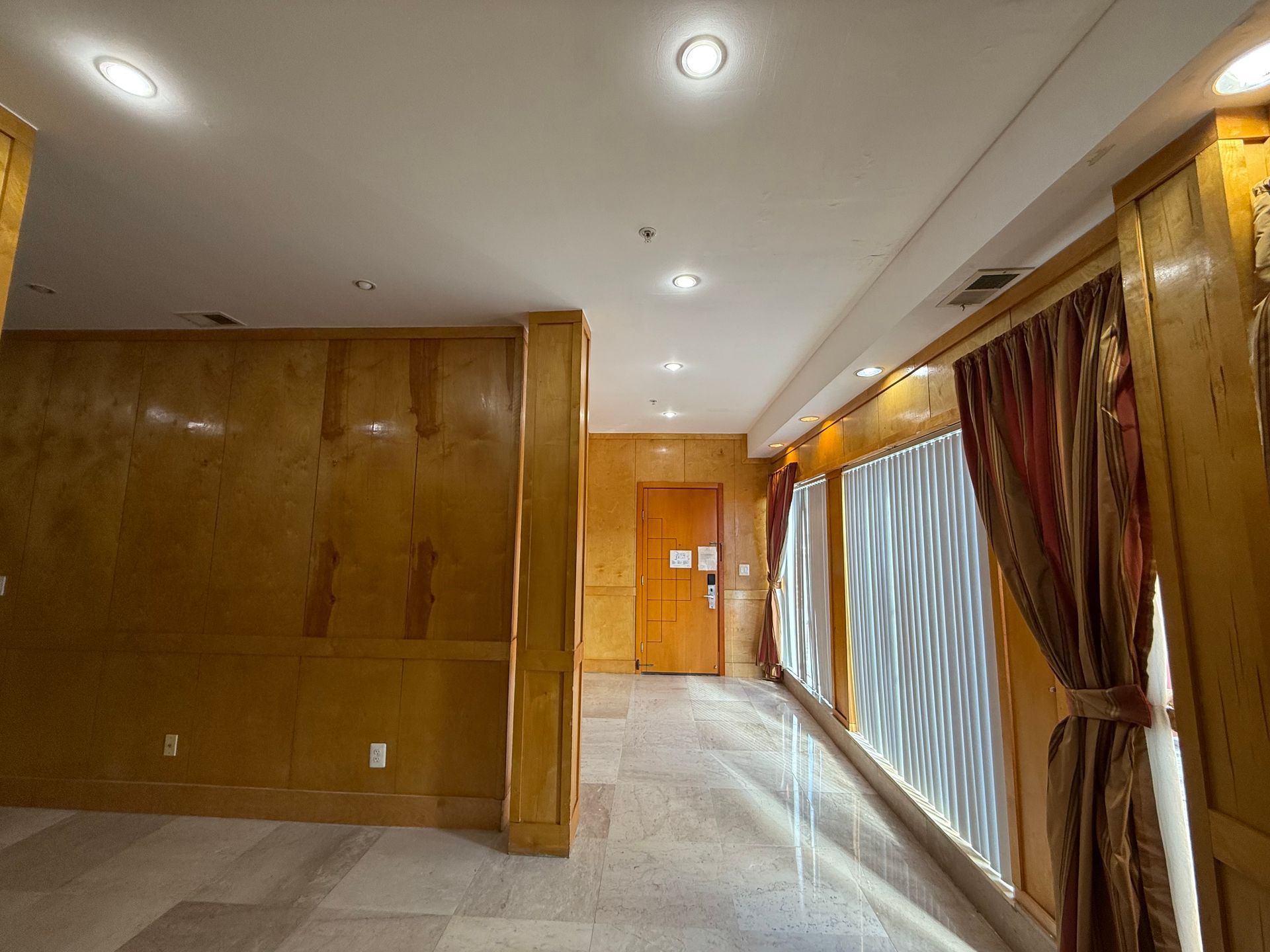 Interior with wood paneling, large windows with curtains, and a door at the end of the hallway.