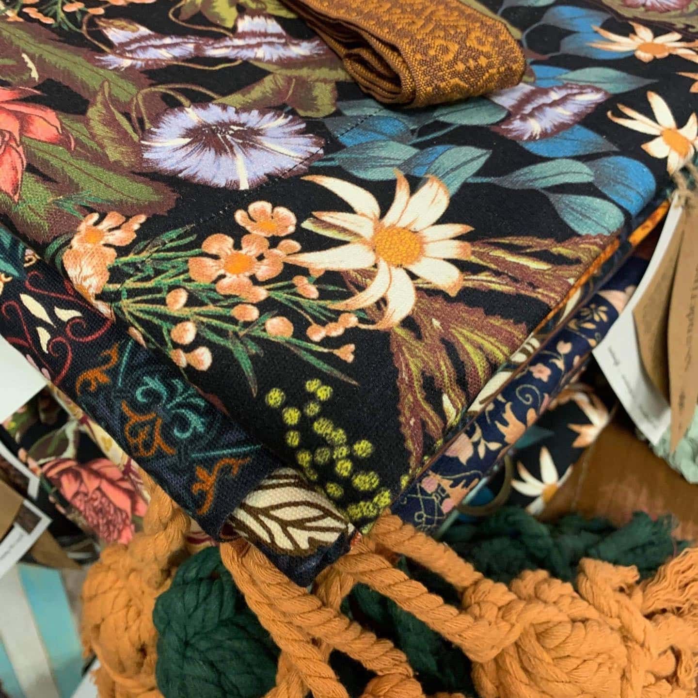 Pile of Floral Fabric in Dark Colours, With Orange Tassel and Trim — Decadence Gifts & Homewares in Yeppoon, QLD